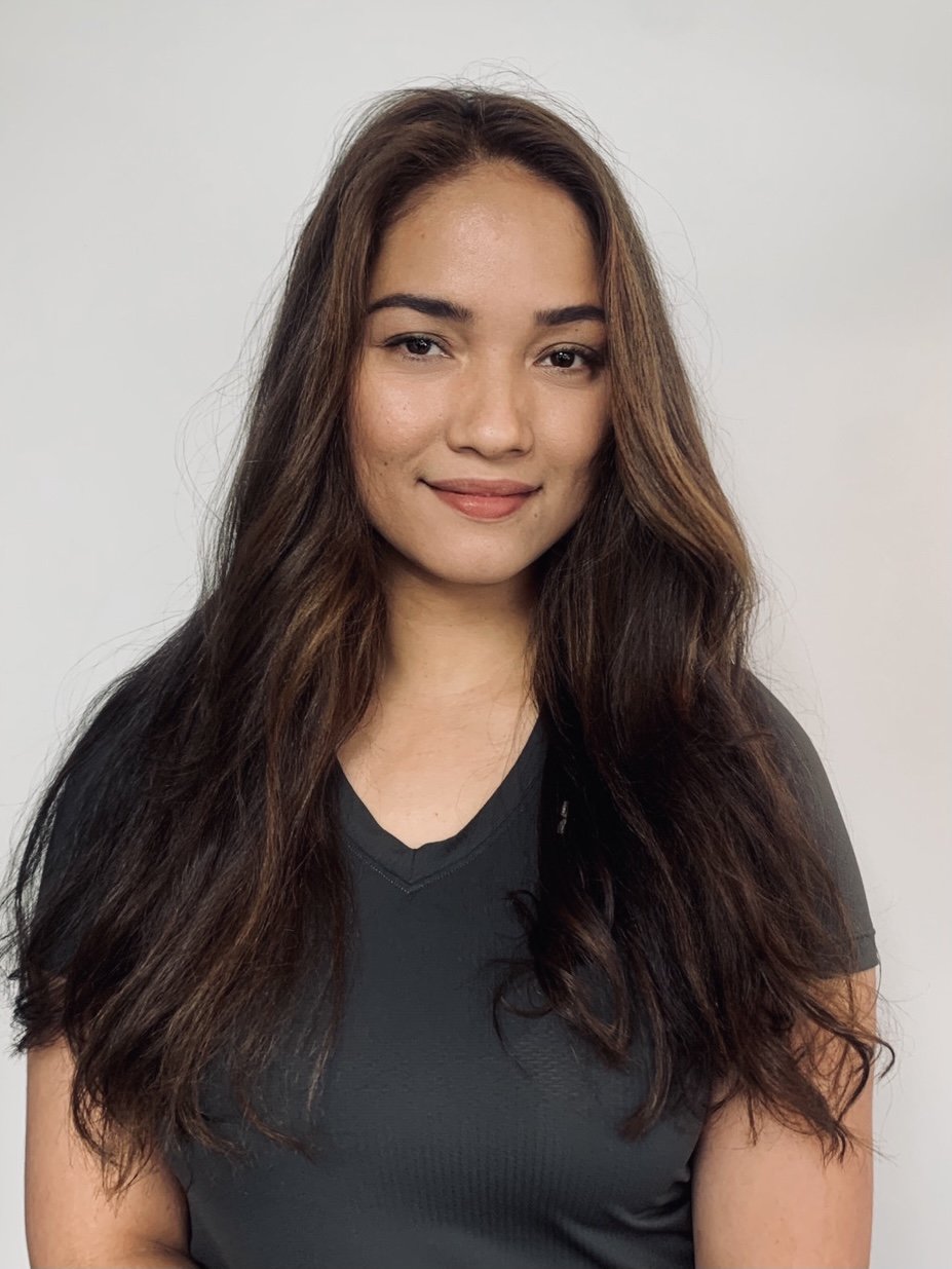 Portrait of a woman with long hair wearing a dark shirt, smiling against a plain background.