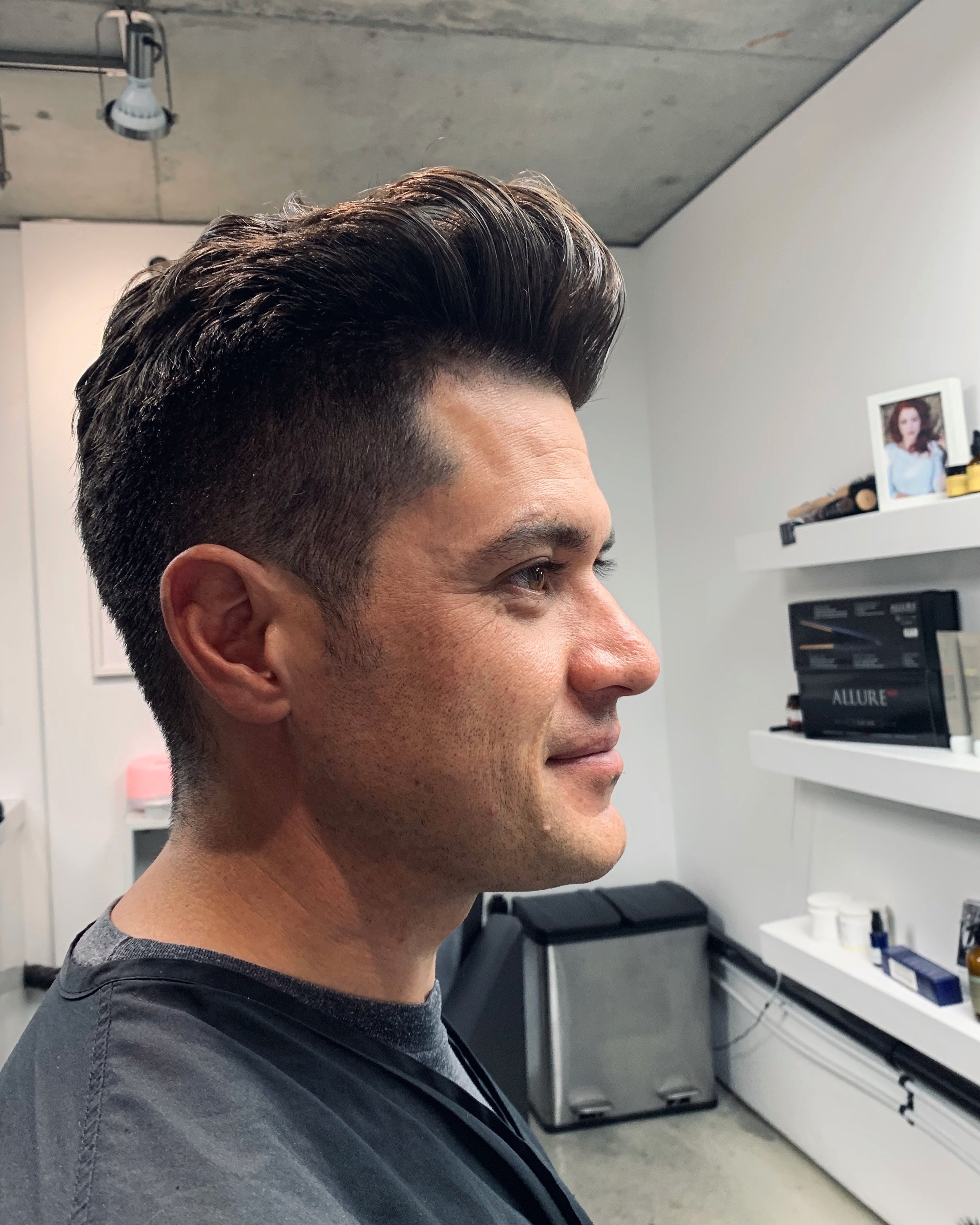 Side profile of a man with dark, styled hair in a salon or barbershop.