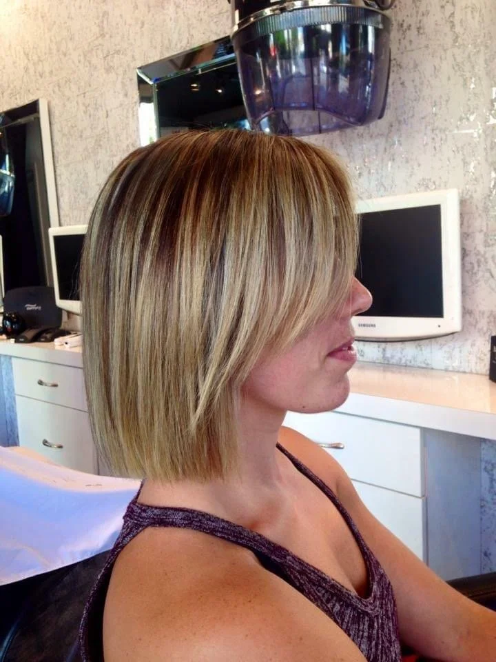 Woman with shoulder-length, blonde layered hair in a salon or barbershop setting.