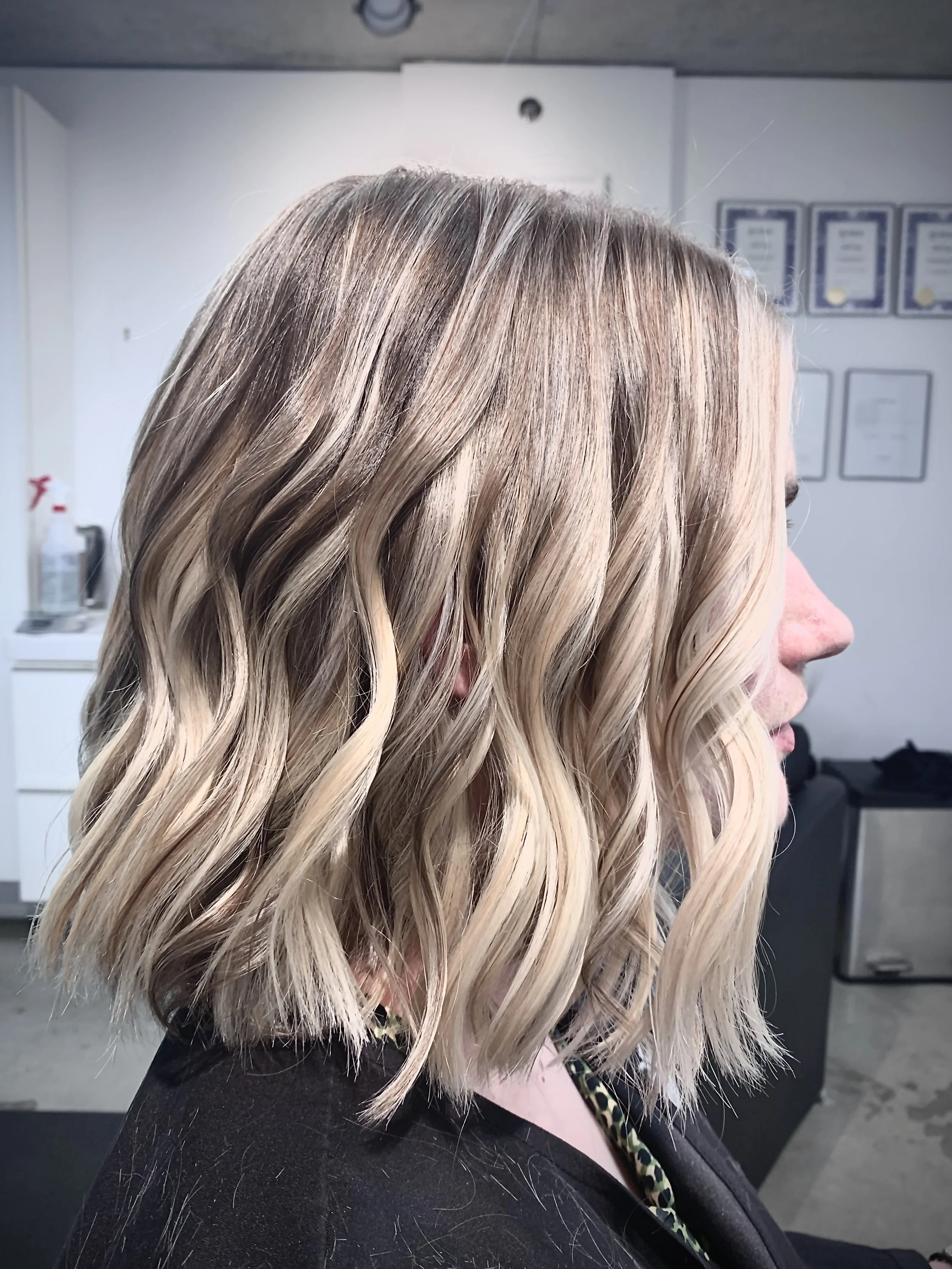 Side profile of a person with wavy blonde hair in a salon.