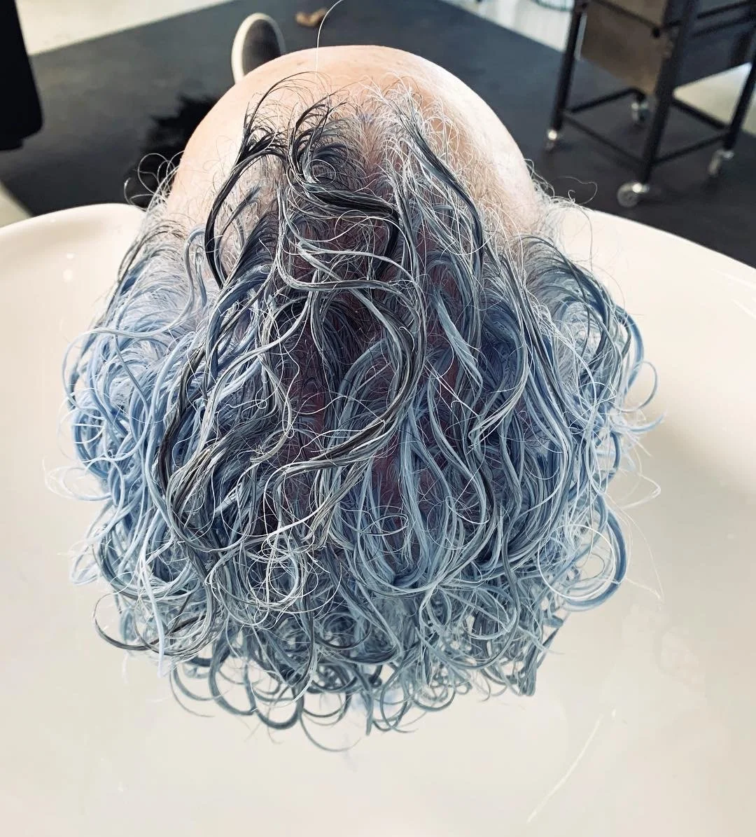 Close-up of a person's head with short curly hair dyed bluish-gray