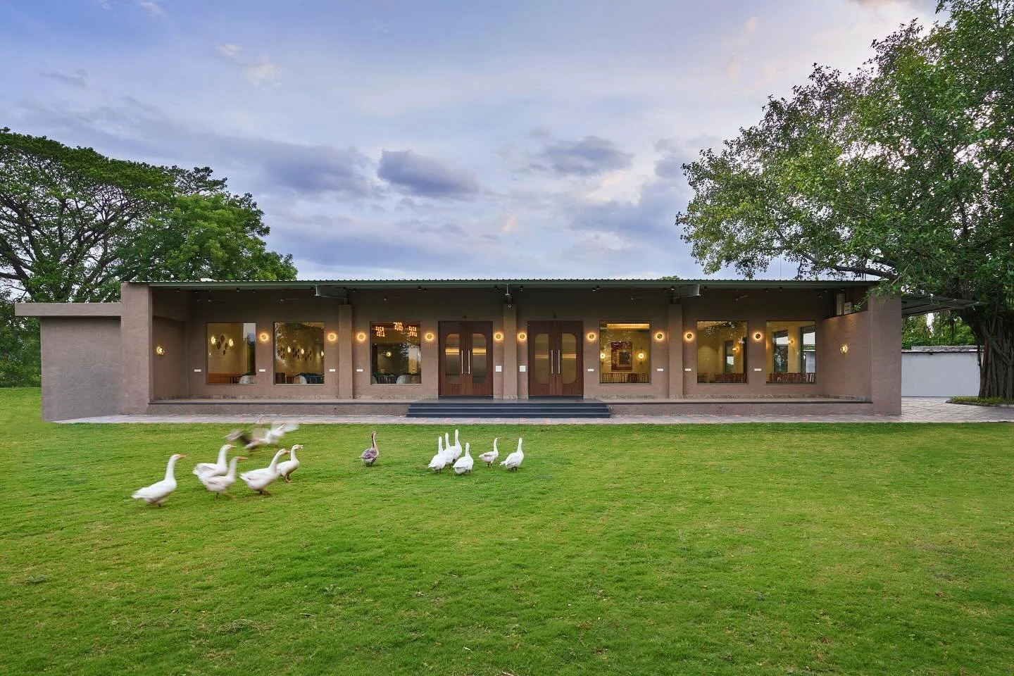 The structure, with its cleaned lines and earth-toned facade,offers a harmonious connection to its surroundings. Large windows and ambient lighting inside creates a seamless flow between exterior and interior while making the structure stand bold. 


