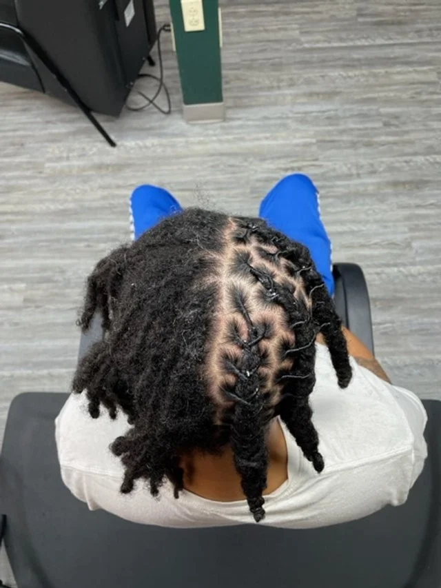 A person with dreadlocks sitting in a salon chair, viewing their hairstyle from above.