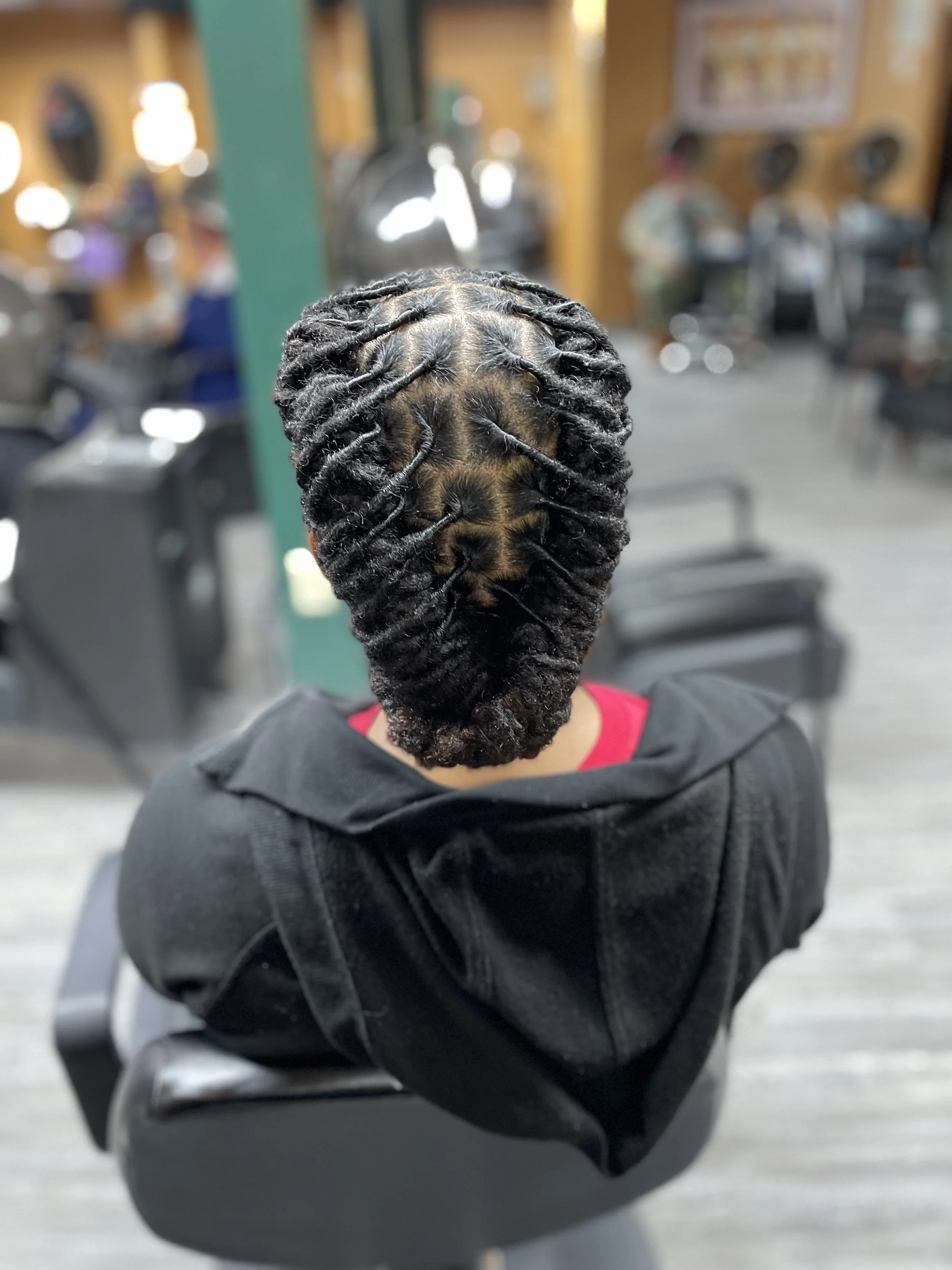 Back view of a person with freshly styled, thick, black, twisted locs in a salon or barbershop.