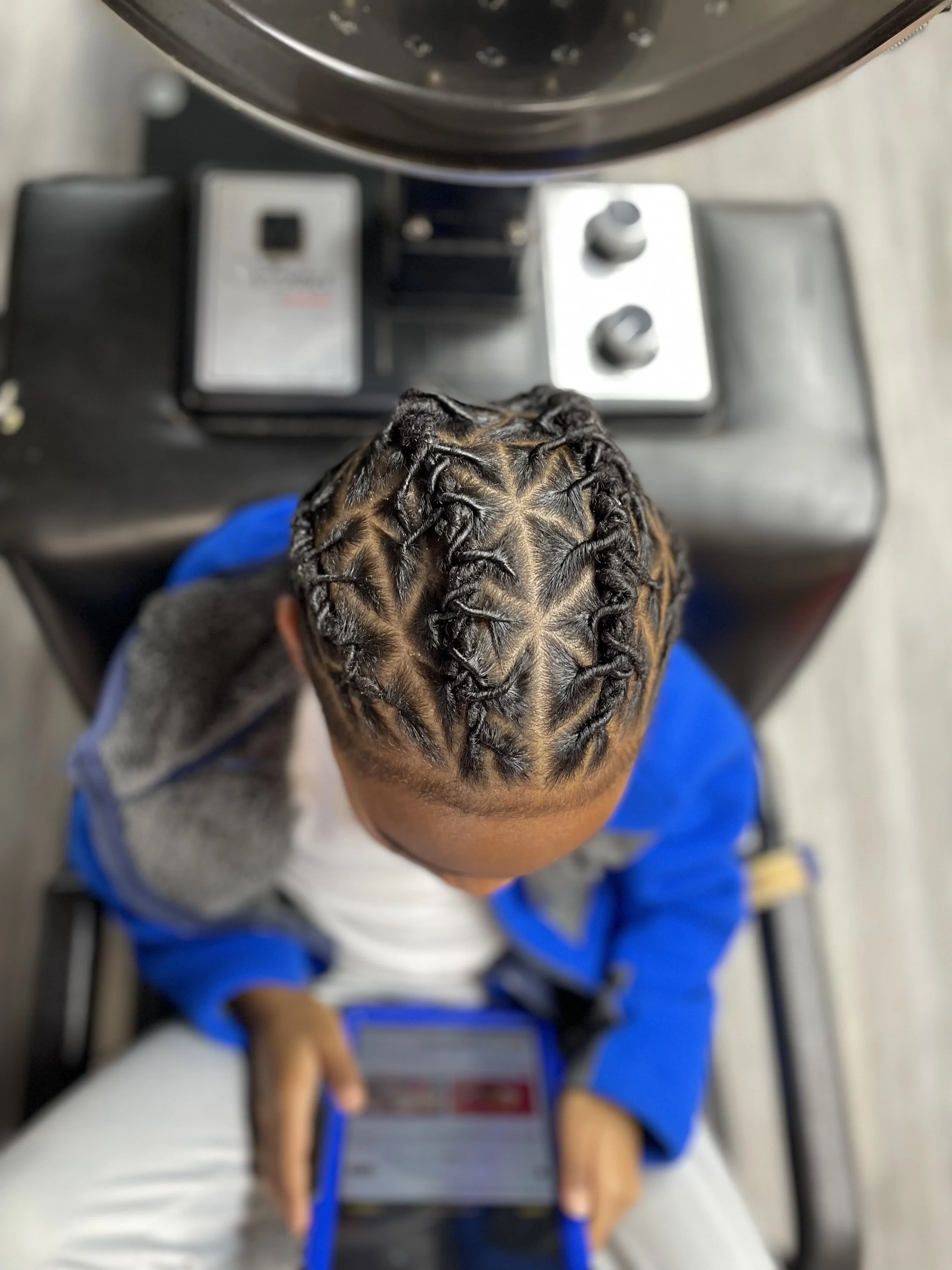 Top view of a person with braided hairstyle, sitting on a chair, holding a tablet, with an electronic device on a table in front of them.