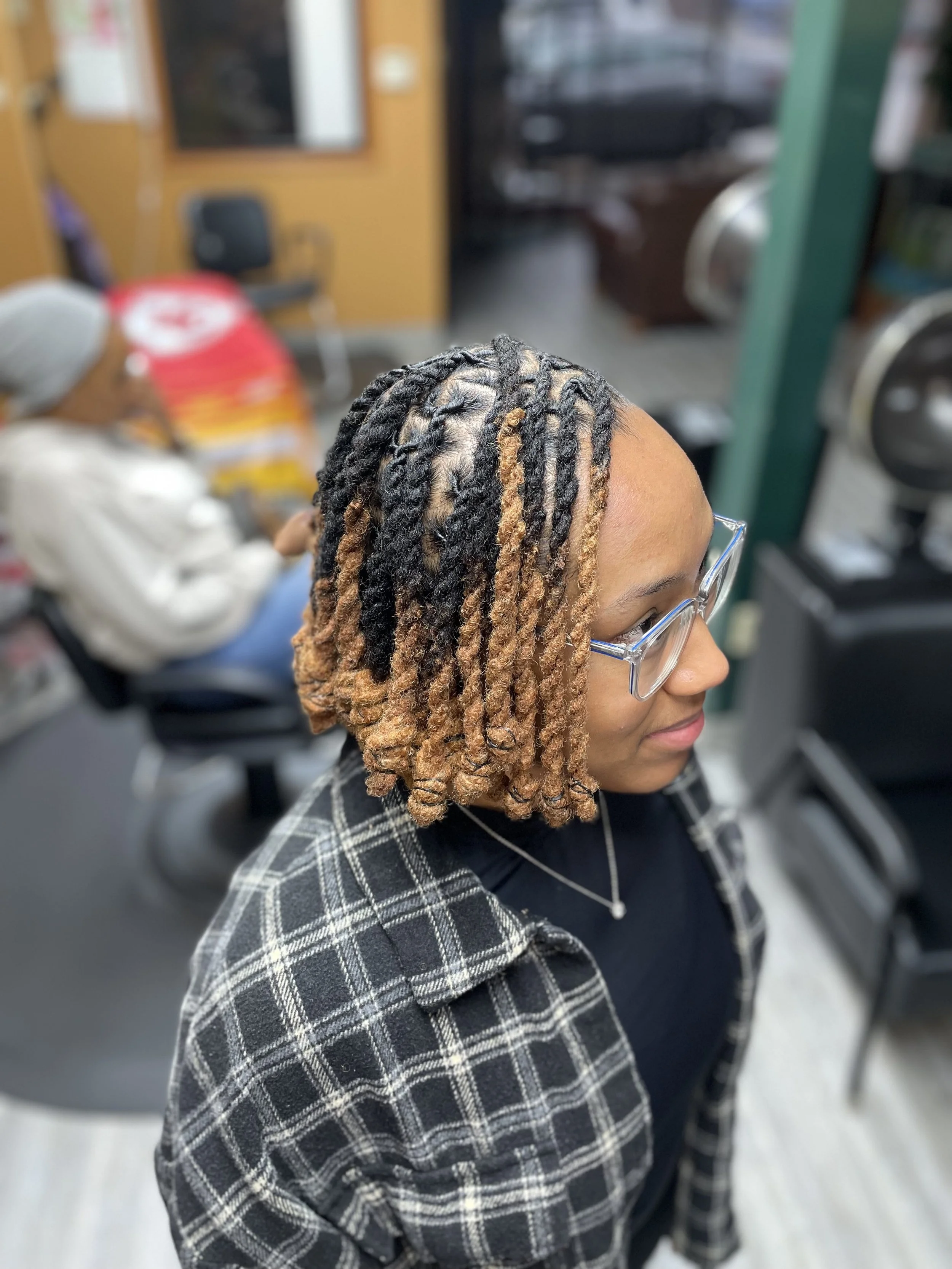 Woman with glasses and shoulder-length dreadlocks with black and blonde tips sitting in a salon.