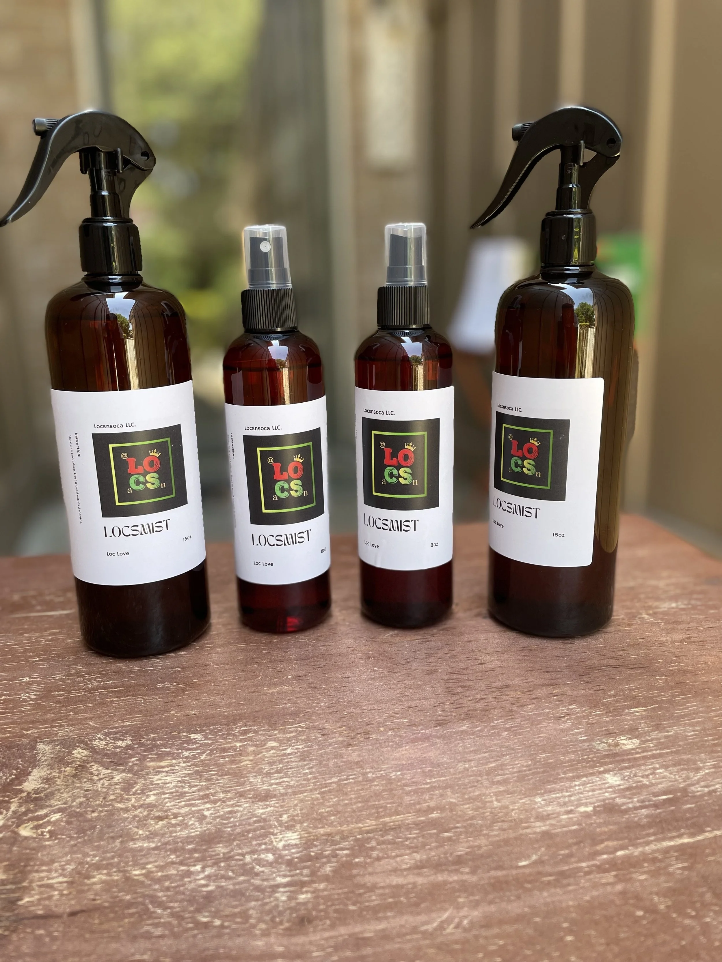 Four brown spray bottles labeled 'LOCSMIST' with different sizes are arranged on a wooden surface, with a blurred background showing a window with greenery outside.