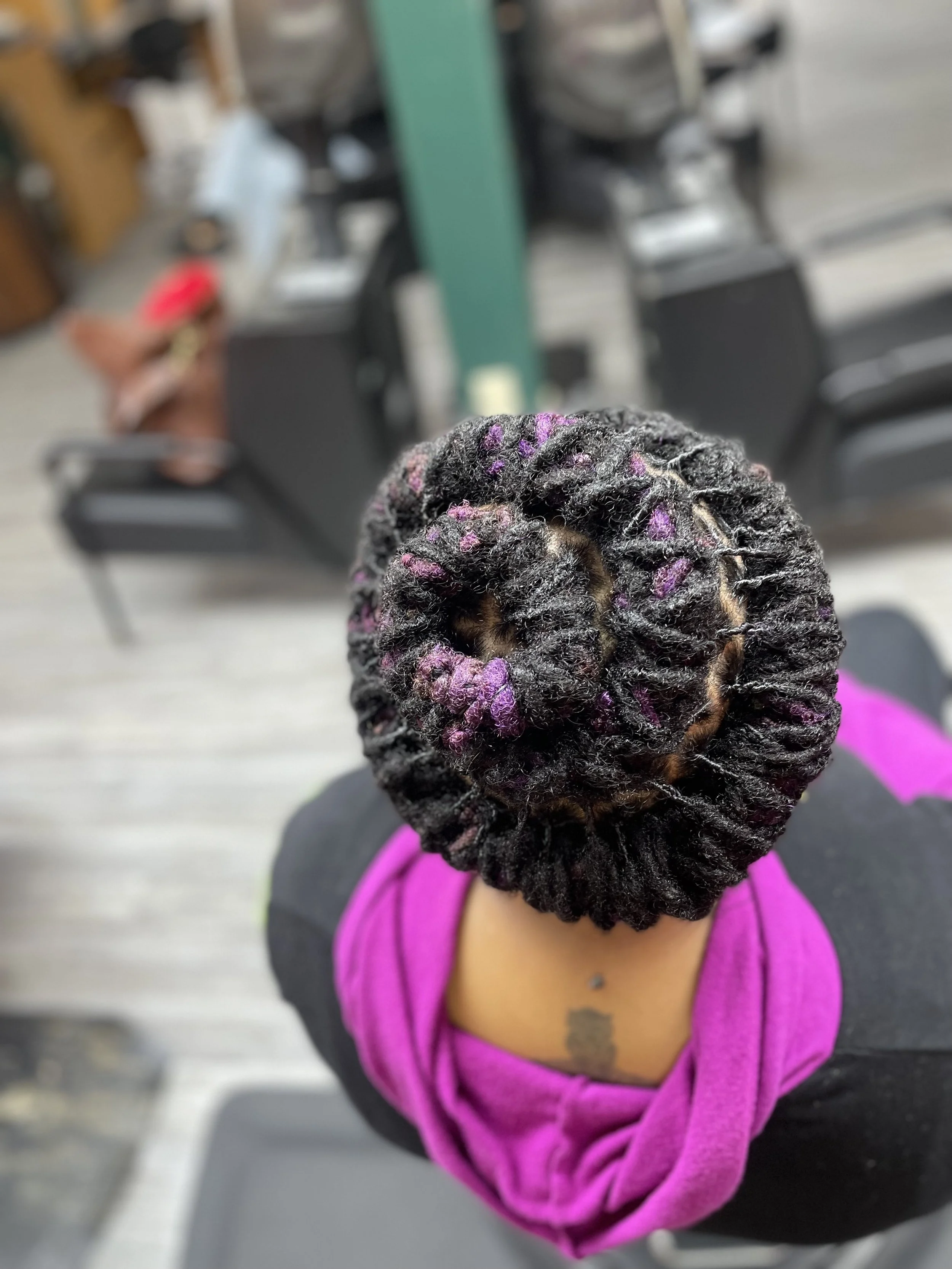 Top view of a person's head with black locs wrapped in a black and purple headscarf.