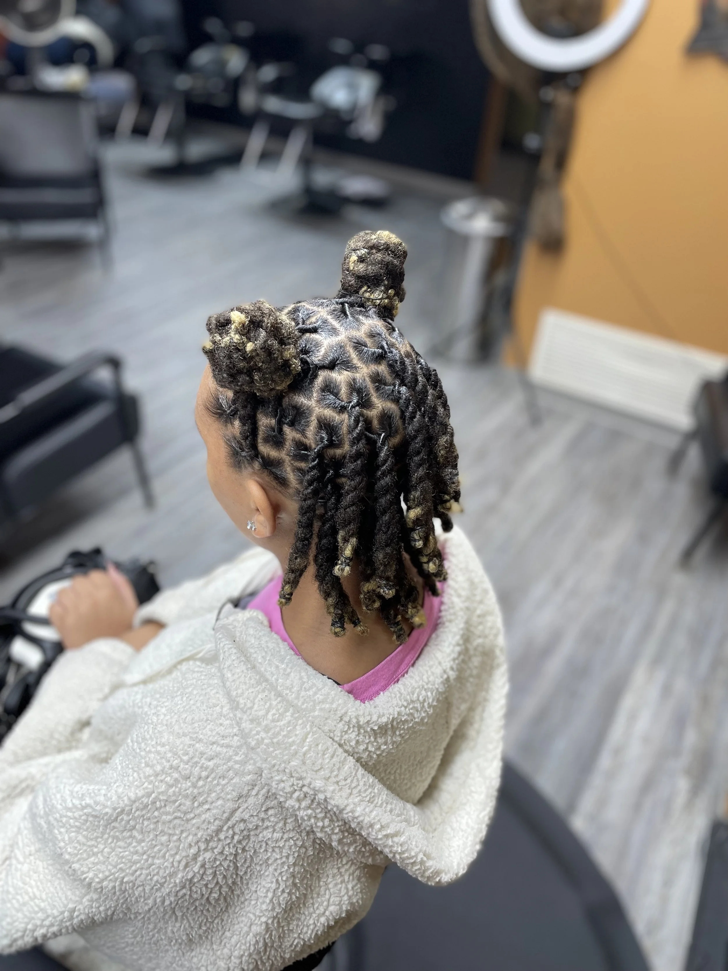 A woman with styled dreadlocks featuring small buns on top, sitting in a salon chair.