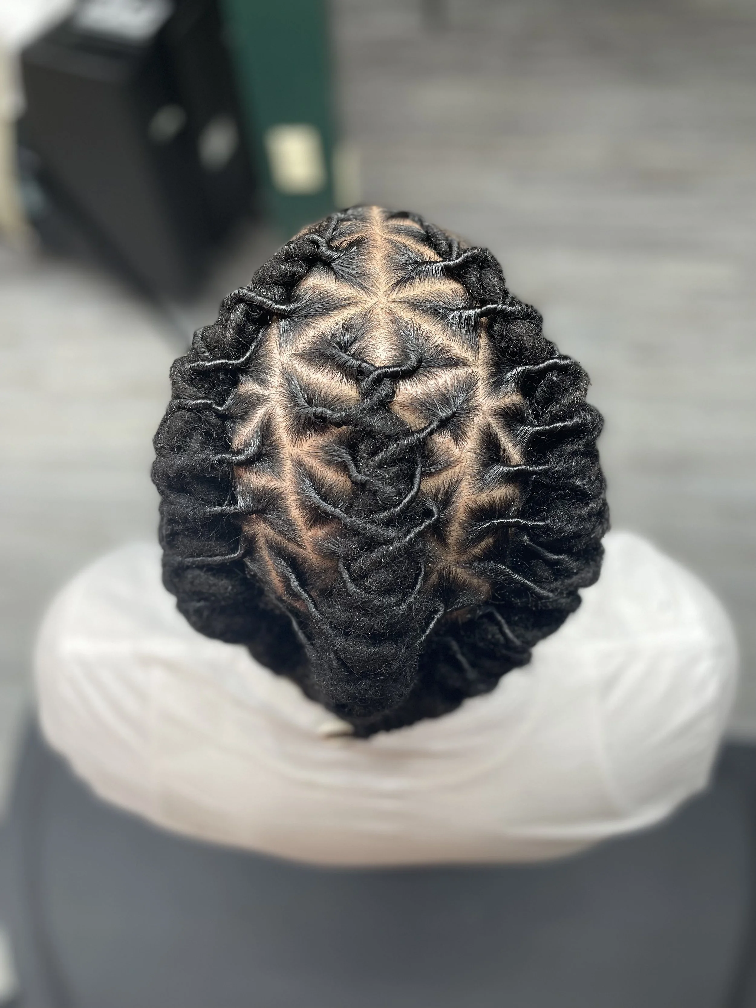 Top view of a head with neatly styled black locs tightly woven in an intricate pattern.