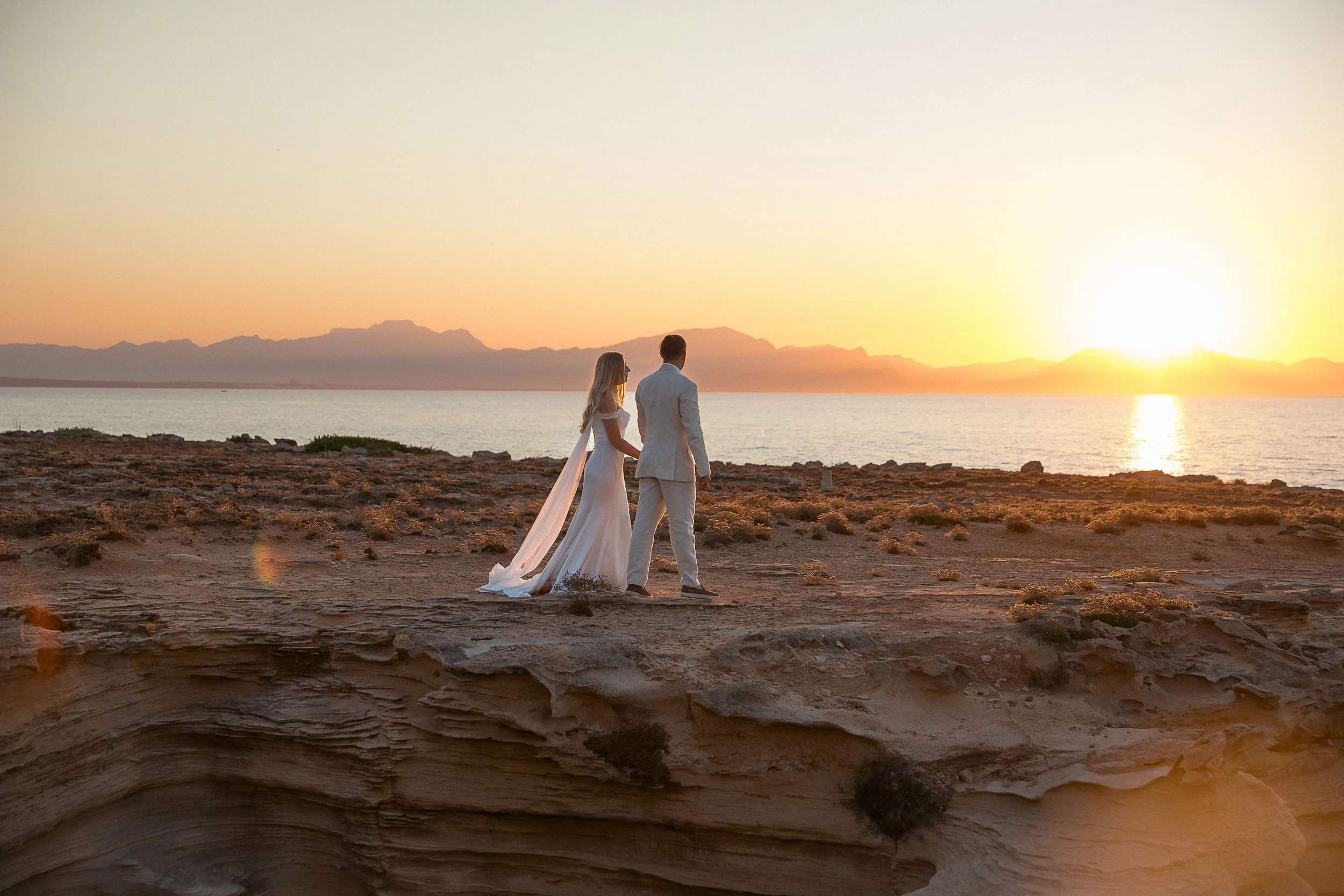 A bride and groom walk cliffside at sunset during their elopement in Mallorca