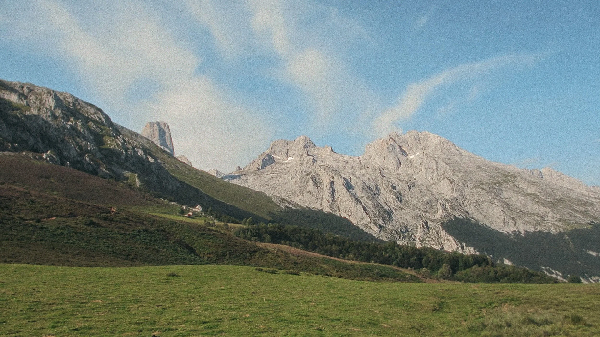 An open alpine meadow at Collado Pandébano, with stone mountain towers in the background.