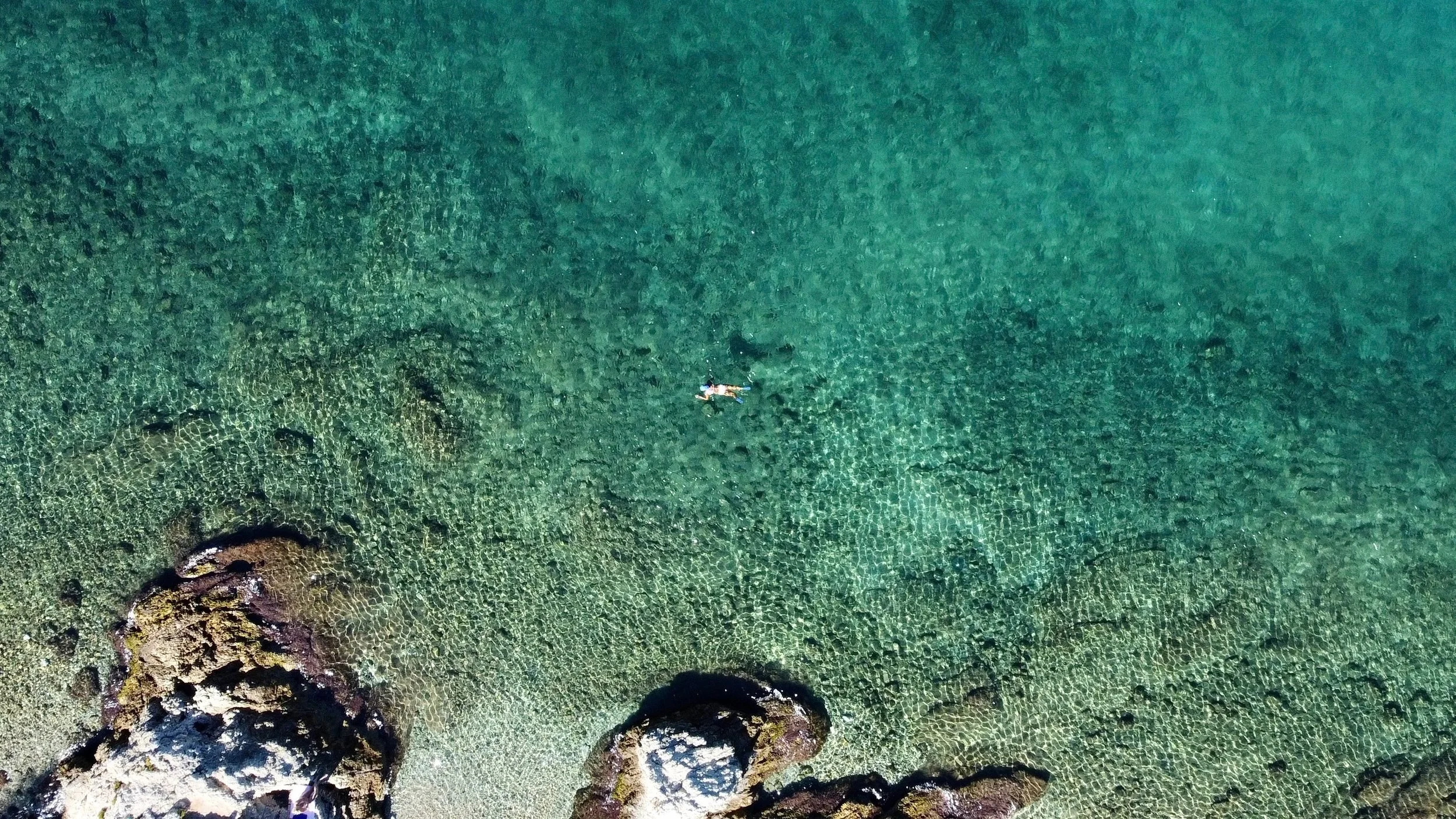 A top down photo of a single female swimming in the clear turquoise green sea by Faliraki, a short drive from Villa Icarus Corfu