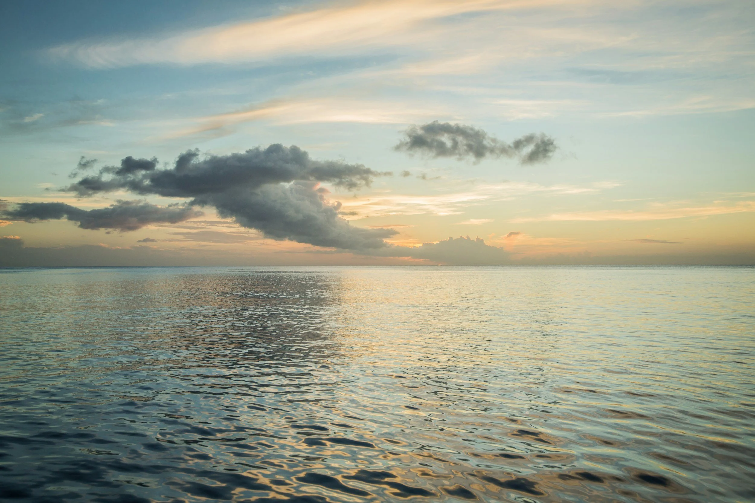 A serene ocean scene during sunset with a sky filled with clouds and calm water reflecting the sky's colors.