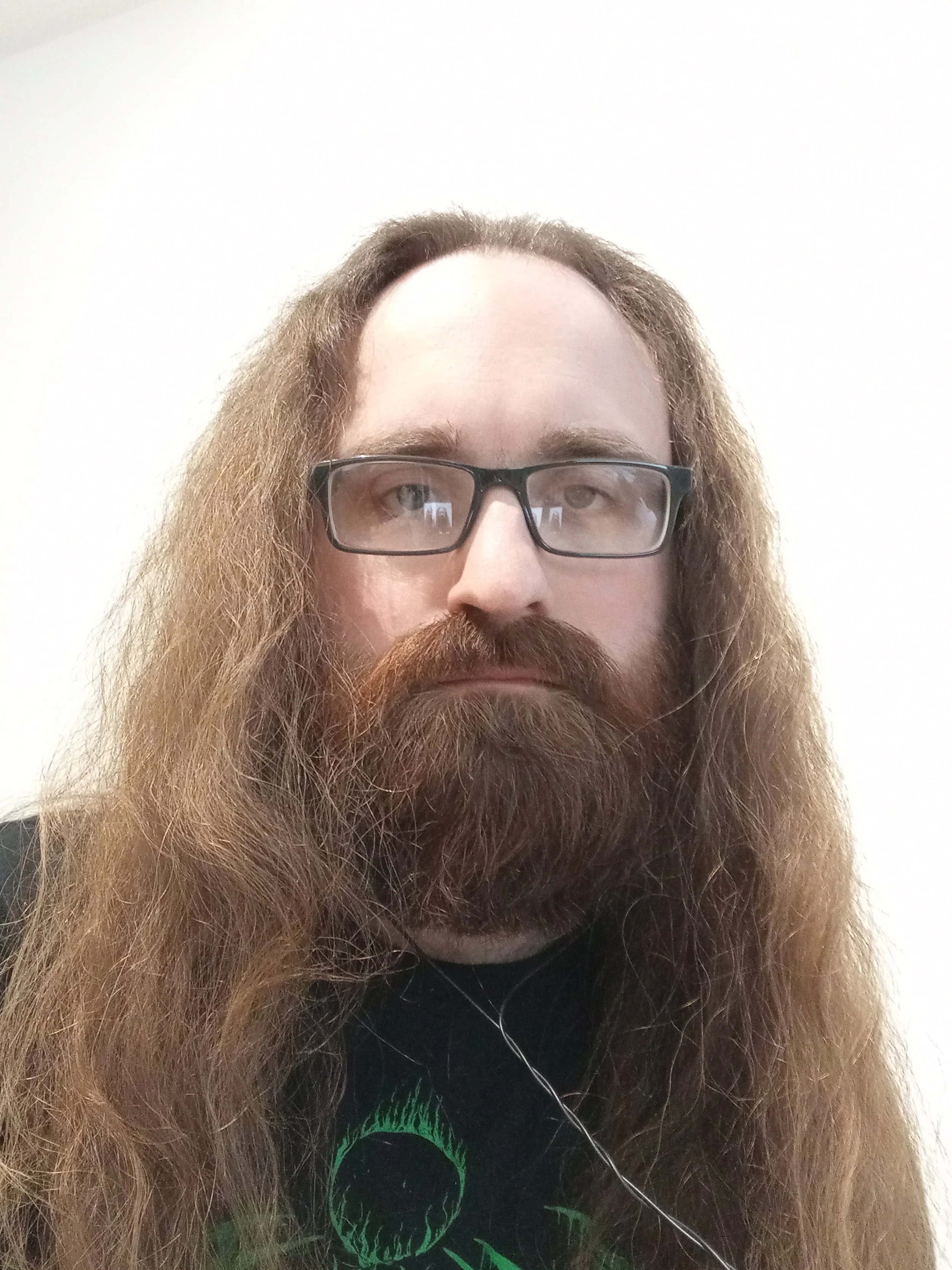 A man with long hair and glasses looks at the camera. The picture shows head, shoulders, and upper chest against a white background.