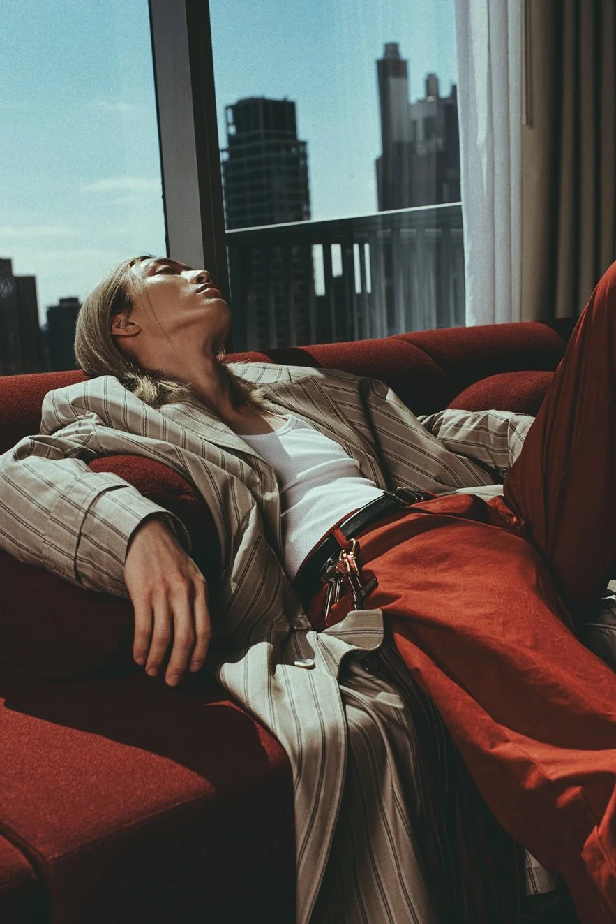 A woman resting on a red sofa near a large window with a cityscape view in the background.