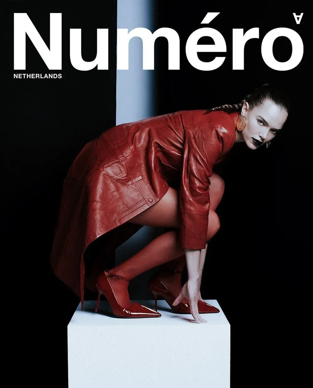 Cover of Numéro magazine featuring a woman in a red leather coat and red high heels, crouching on a white pedestal against a black background.