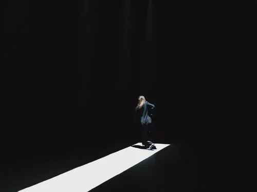 A person standing on a white illuminated path in a dark room with a waterfall in the background.