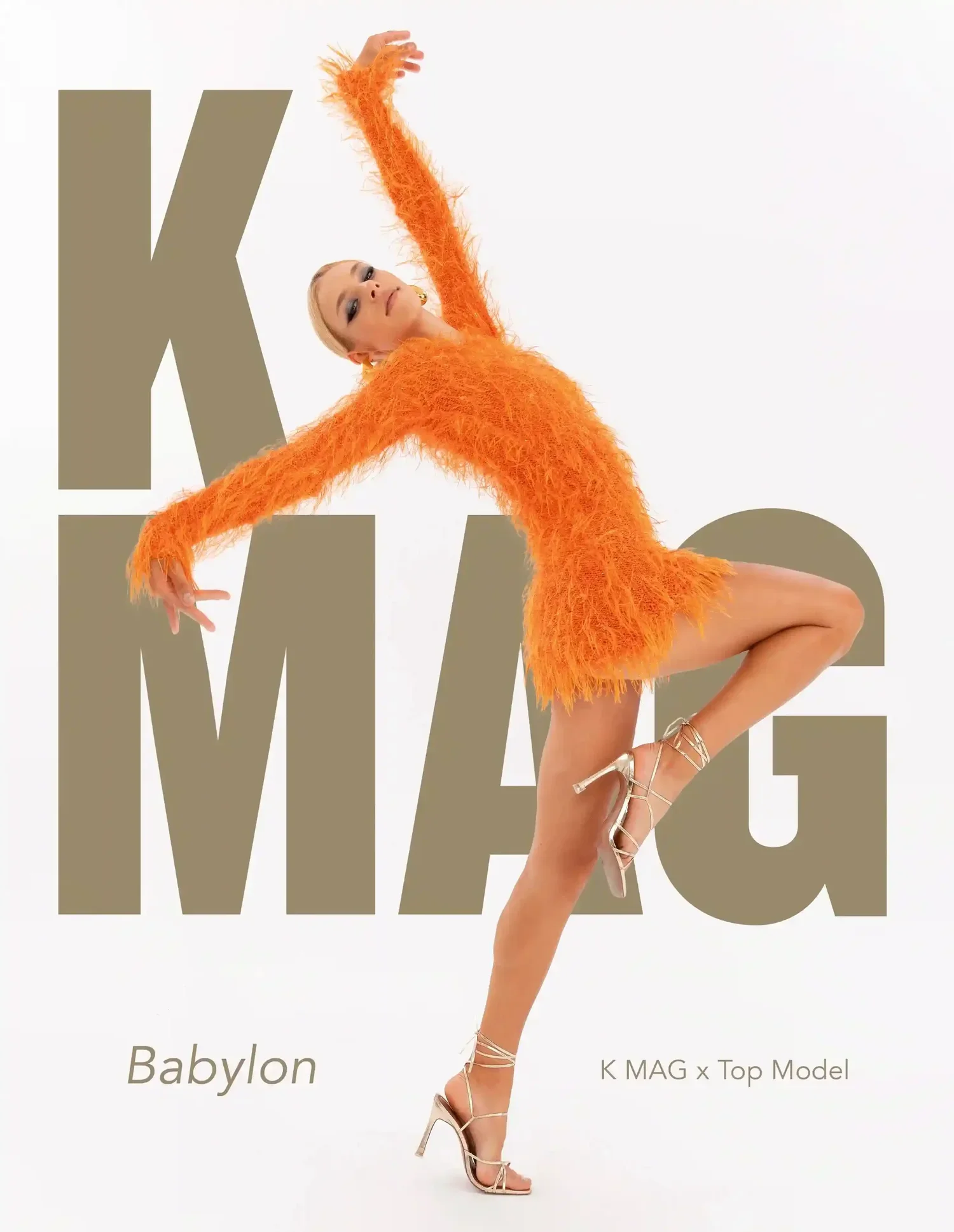 A woman in an orange, fuzzy dress with high heels is striking a dance pose against a white background with large, beige-colored text that says 'K MAG'. The text also includes smaller words 'Babylon' and 'K MAG x Top Model'.