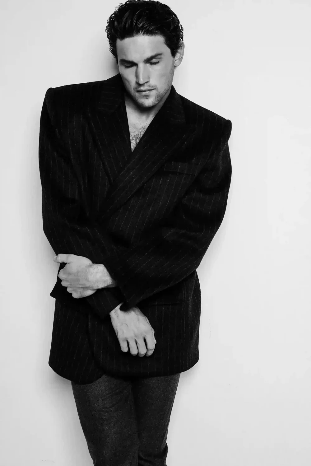 Black and white portrait of a man dressed in a dark pinstripe blazer with a serious expression, standing against a plain white background.