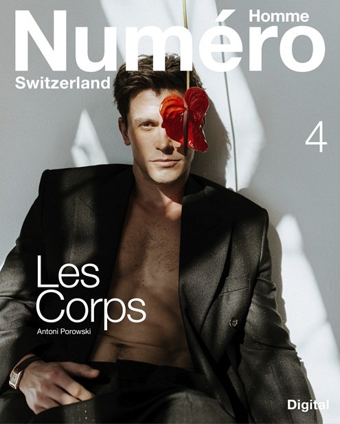 Cover of Numéro Homme Switzerland magazine featuring a shirtless man in a black blazer with a red flower draped over his face, sitting in front of a white background with shadows.