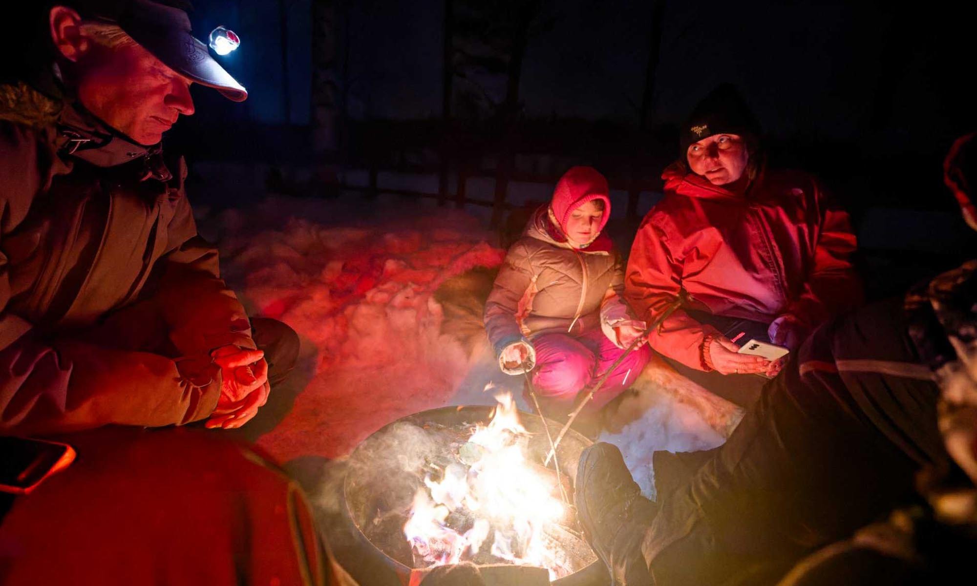 Folk satt vid en mysig eld i snön och åt fika.