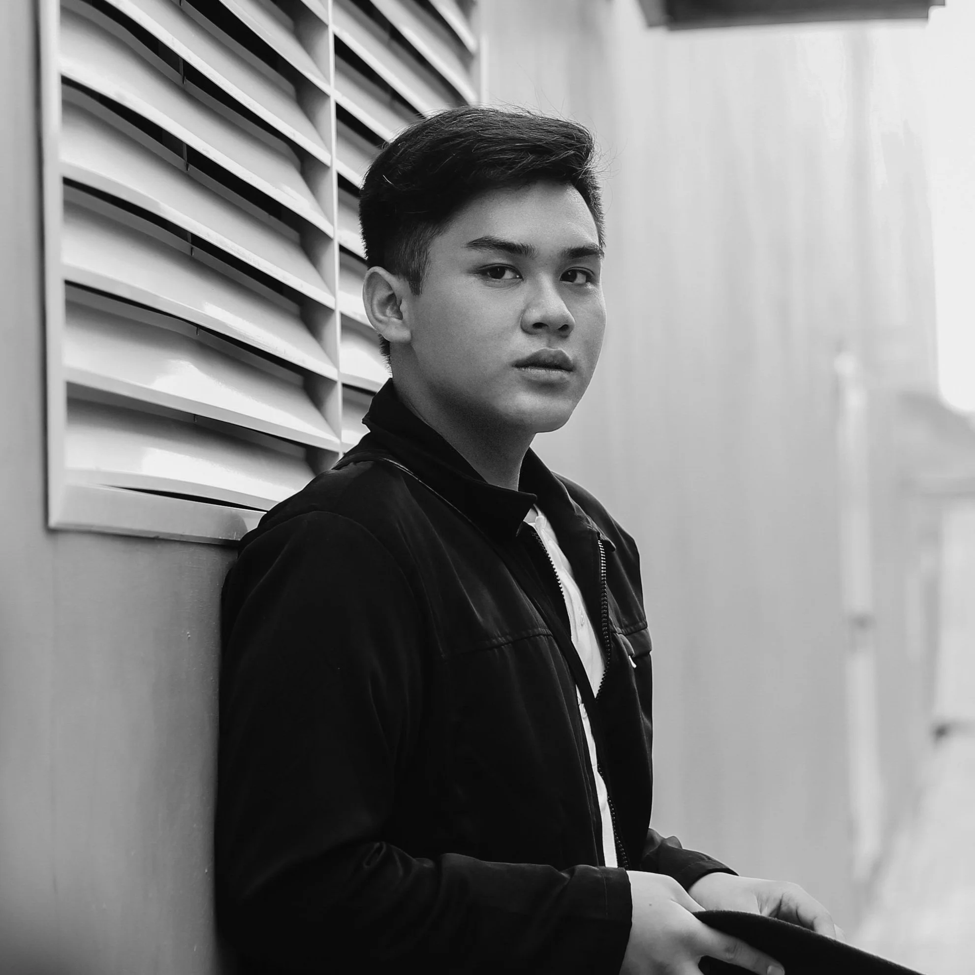Photo of an intense young man dressed in black and wearing headphones, standing in front of a wall and looking into the camera