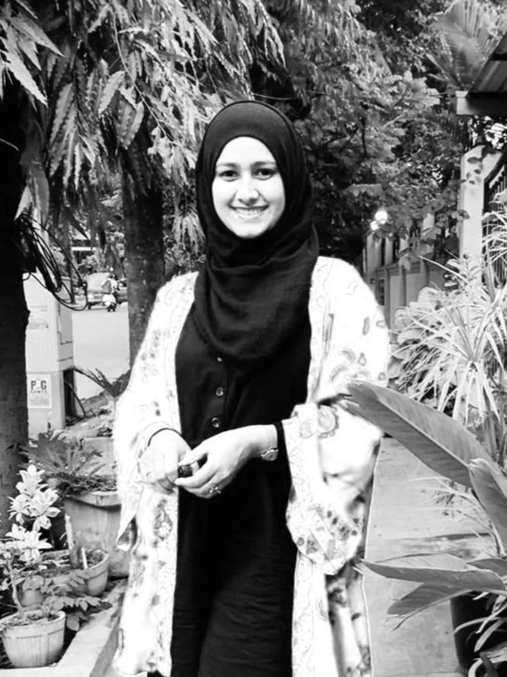 Photo of an elegant smiling woman in a hijab standing in front of greenery