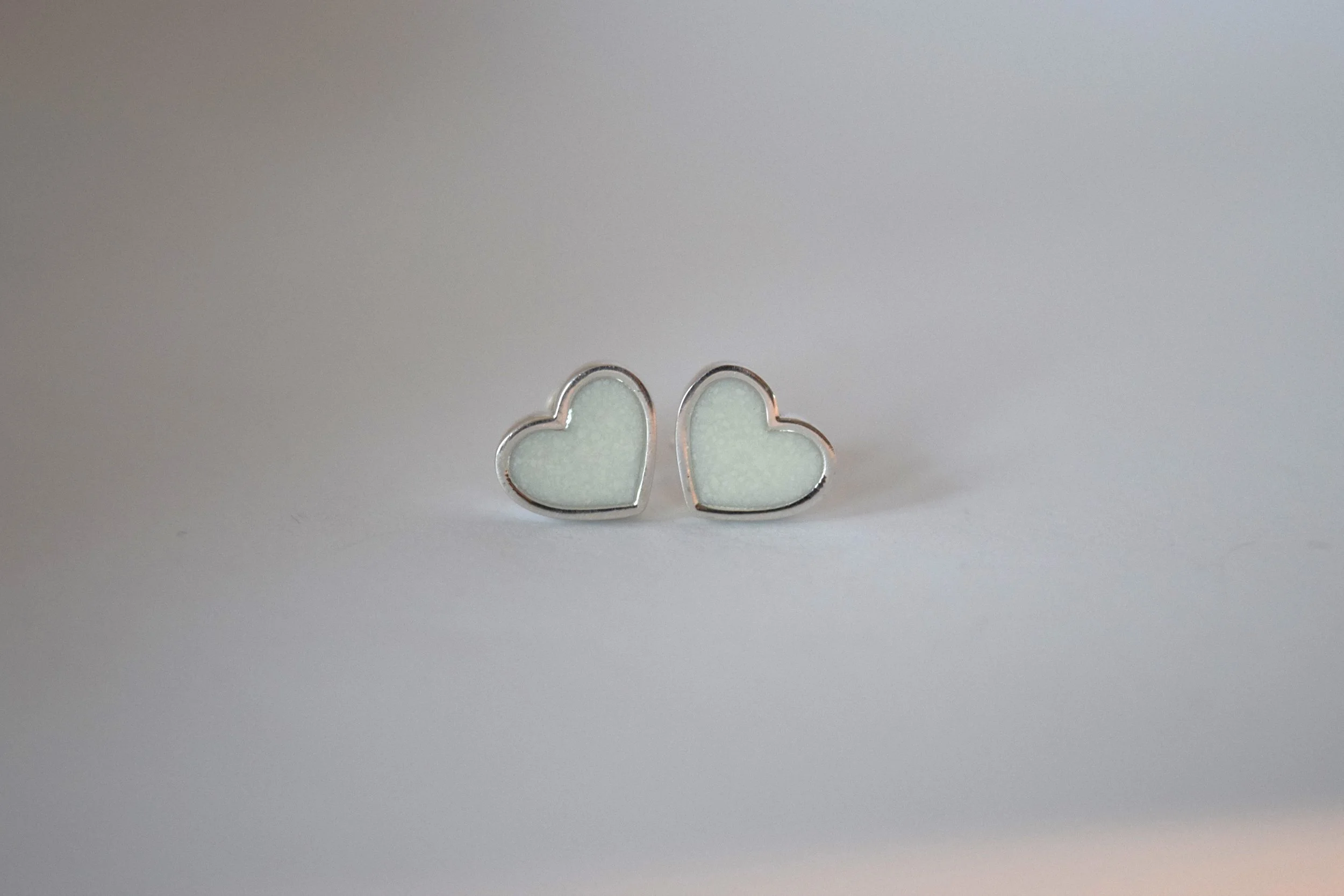 Pair of silver heart-shaped earrings with a pale green interior, placed on a white surface.