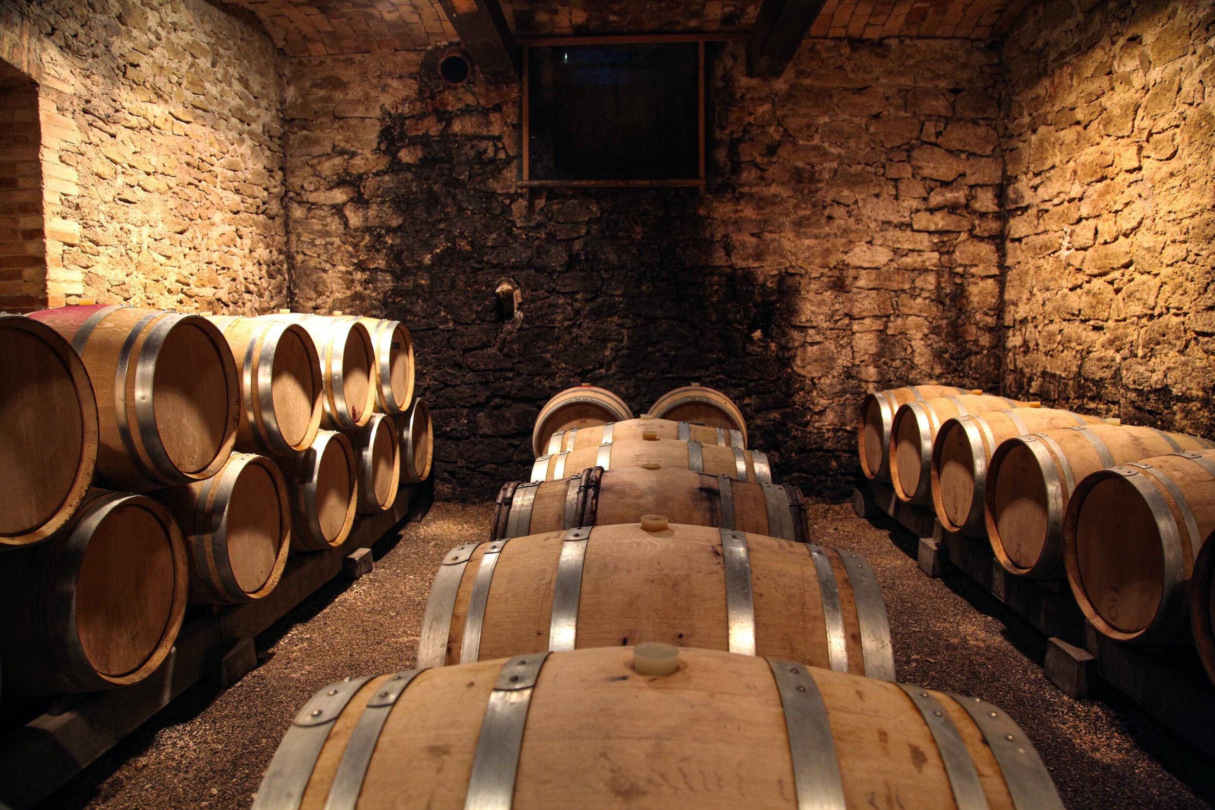 Wine barrels stored in a rustic cellar with exposed stone walls.