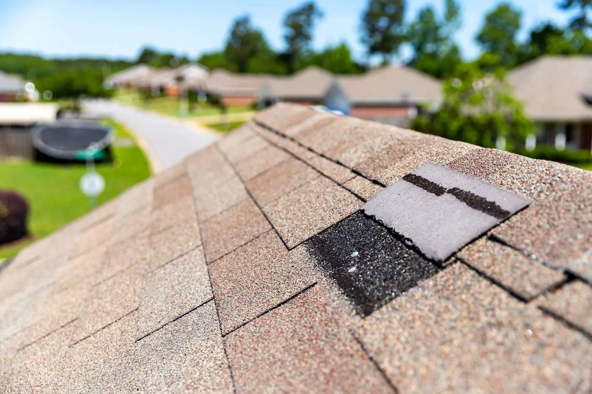 Close-up of a roof with asphalt shingles from atop the roof, showing a shingle with a black sealant or repair patch.