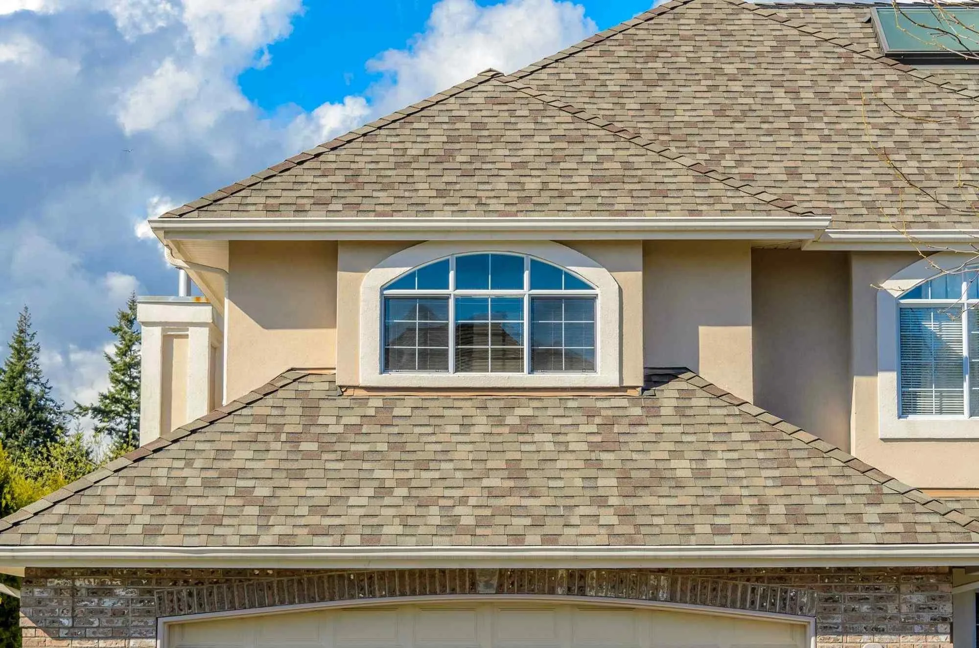 Front view of a house with tan shingle roof, beige stucco walls, and large arched window on the upper level.