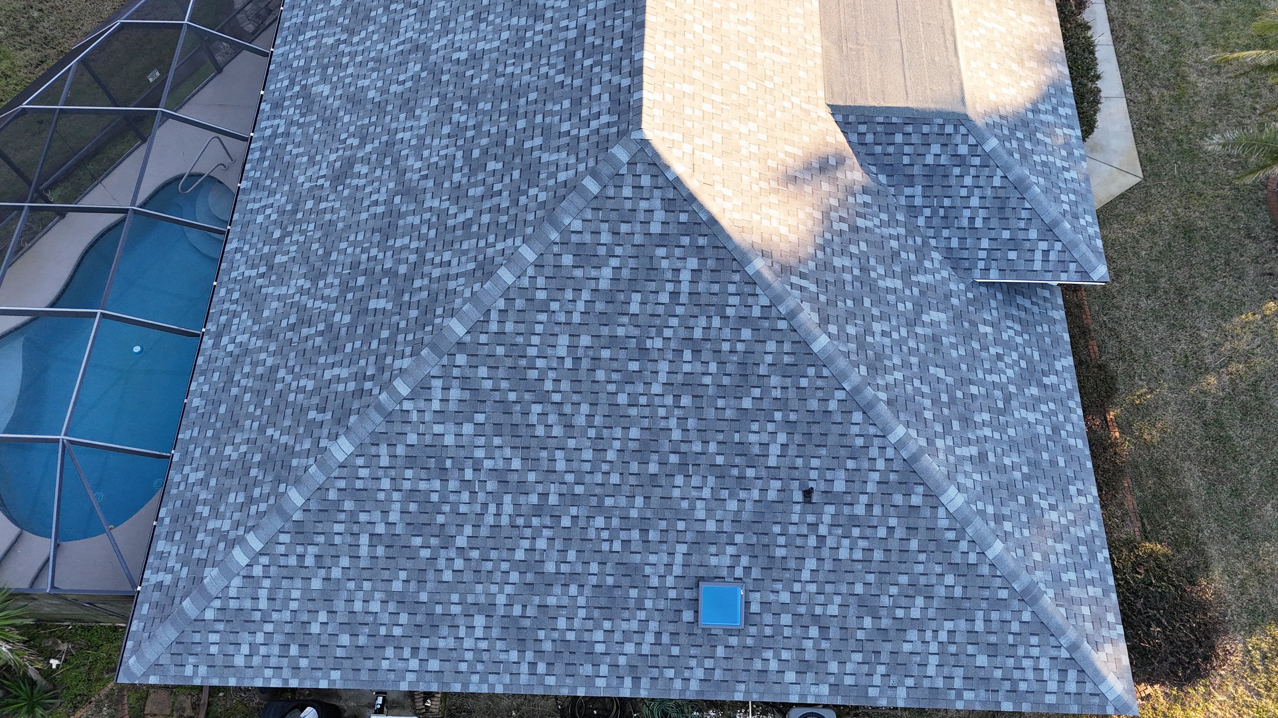 A bird's eye view of a house roof with shingles, a vent, and a section of a screened pool enclosure with a pool inside.