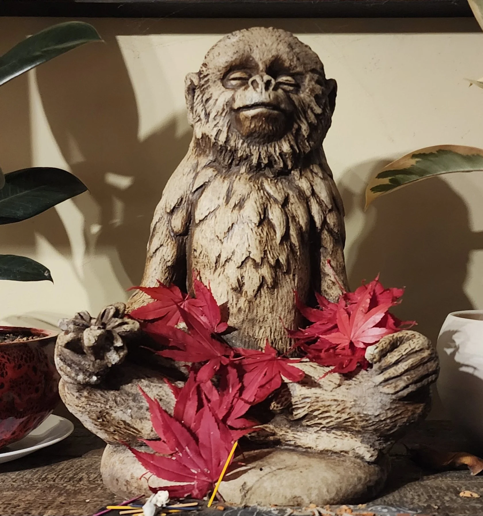 A carved wooden monkey statue sitting in a meditative pose surrounded by red autumn leaves.