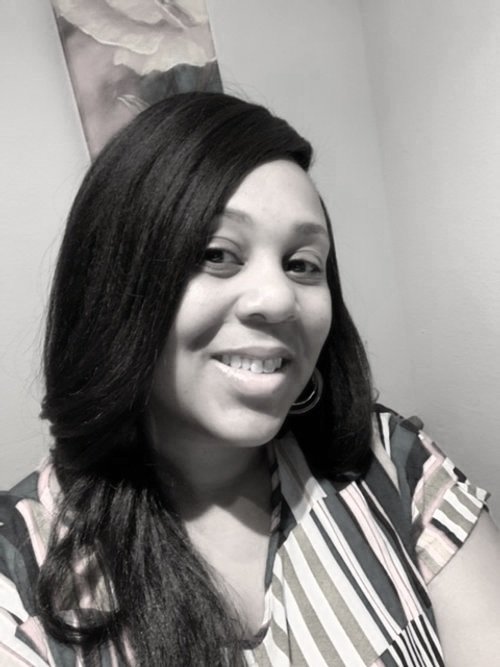 A woman with long dark hair smiling at the camera, wearing a striped shirt, in a room with a picture hanging on the wall.