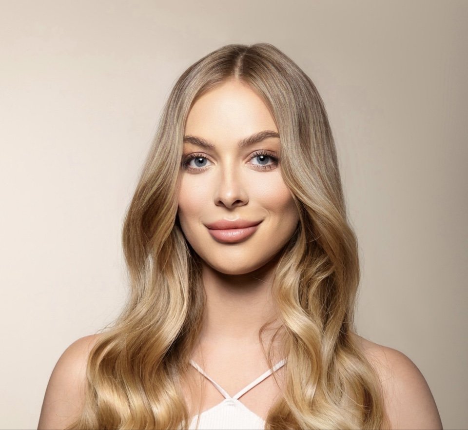 Woman with long blonde hair and light makeup, wearing a white top, smiling.