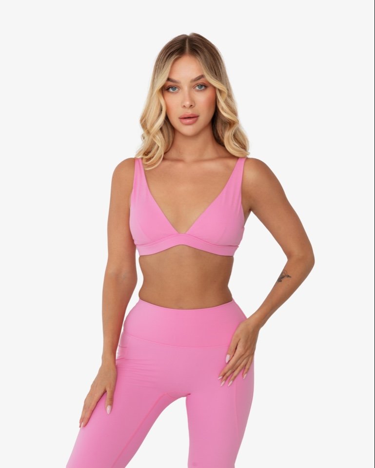 Woman in pink sports bra and leggings posing against white background