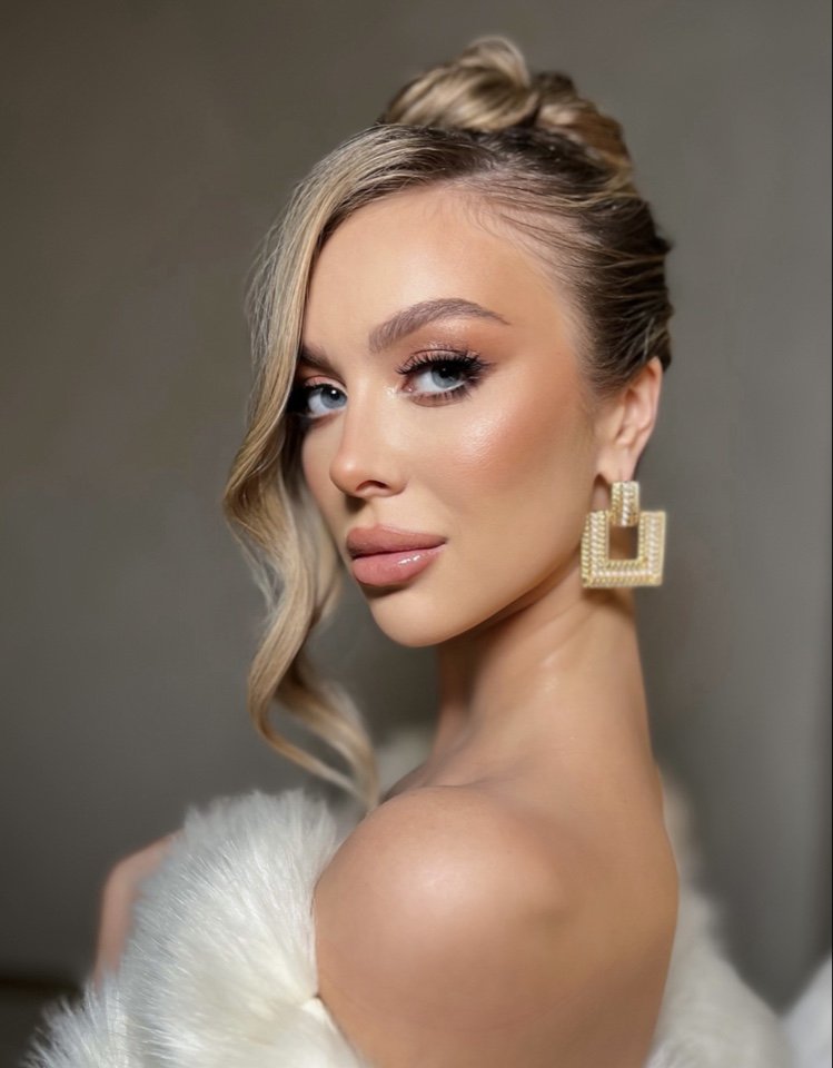 Woman with updo hairstyle, wearing luxury earrings and fur-like garment, looking over shoulder.