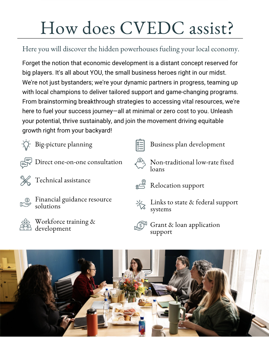 A group of six women sitting around a table in a bright meeting room, engaged in discussion, with documents, laptops, and beverages on the table, and a window with curtains in the background.