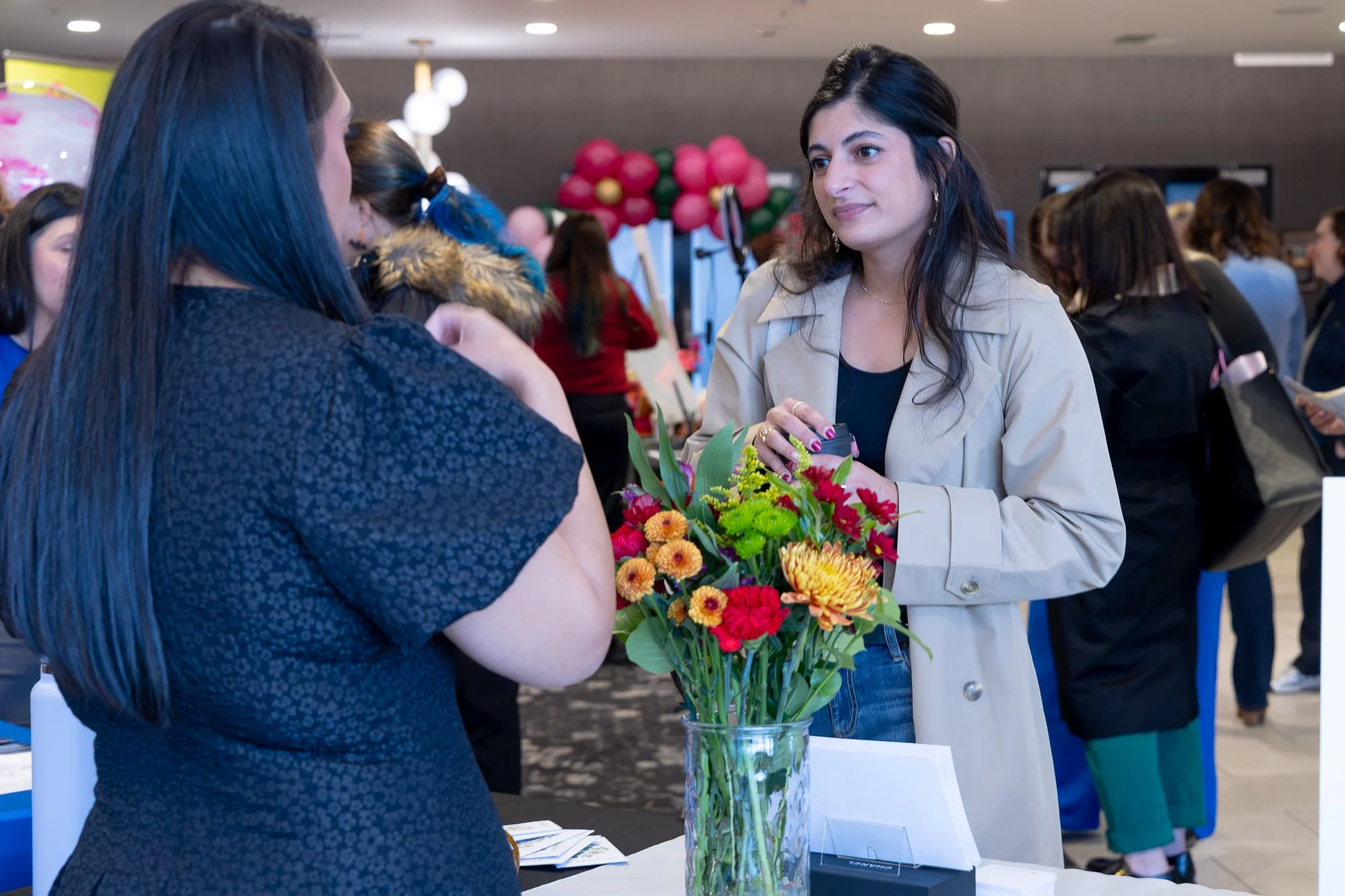 Two women having a conversation at a booth with a bouquet of colorful flowers.