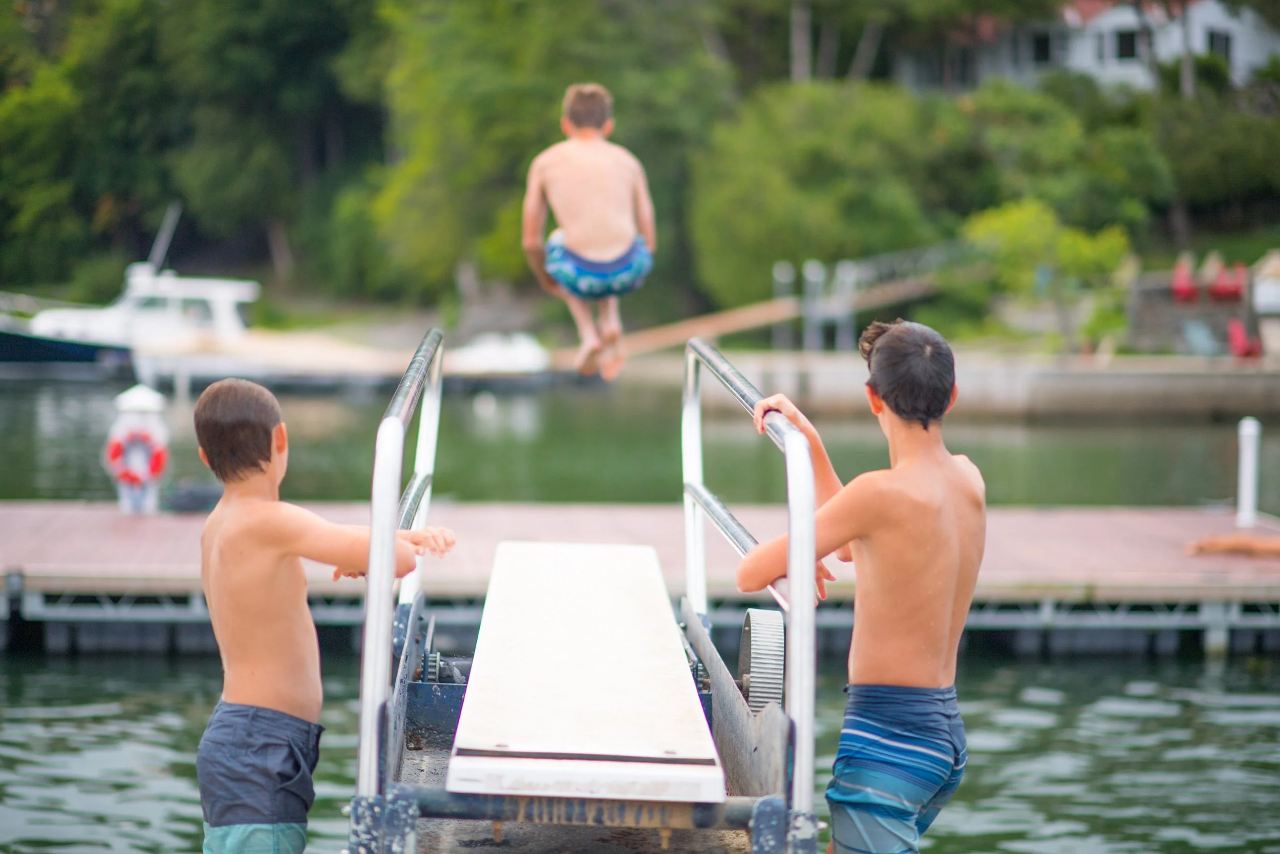 boy does a cannonball off of a diving board while his two friends watch