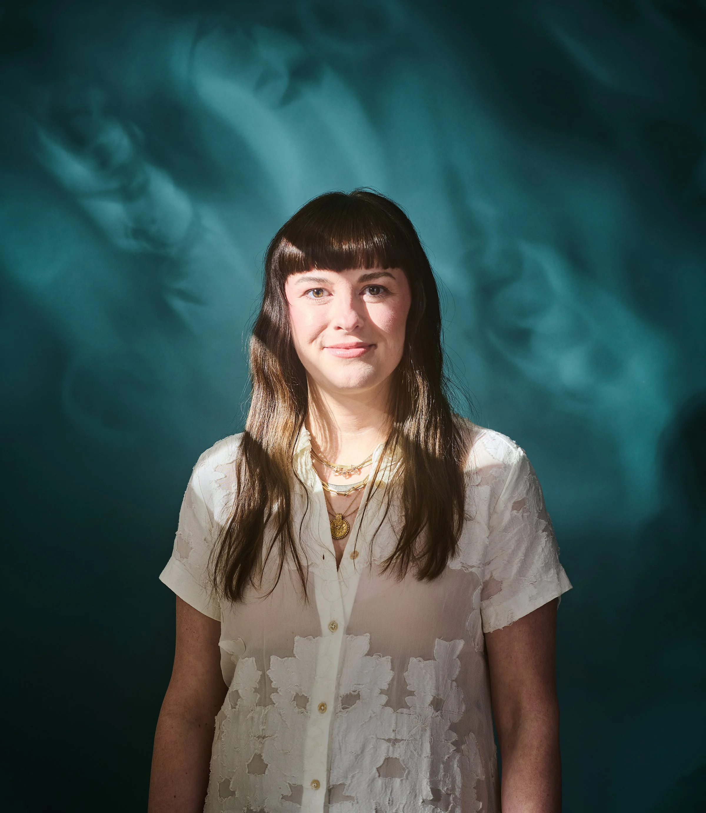 Photo stylist Lizzy Williams wearing a white floral blouse standing against a teal background.