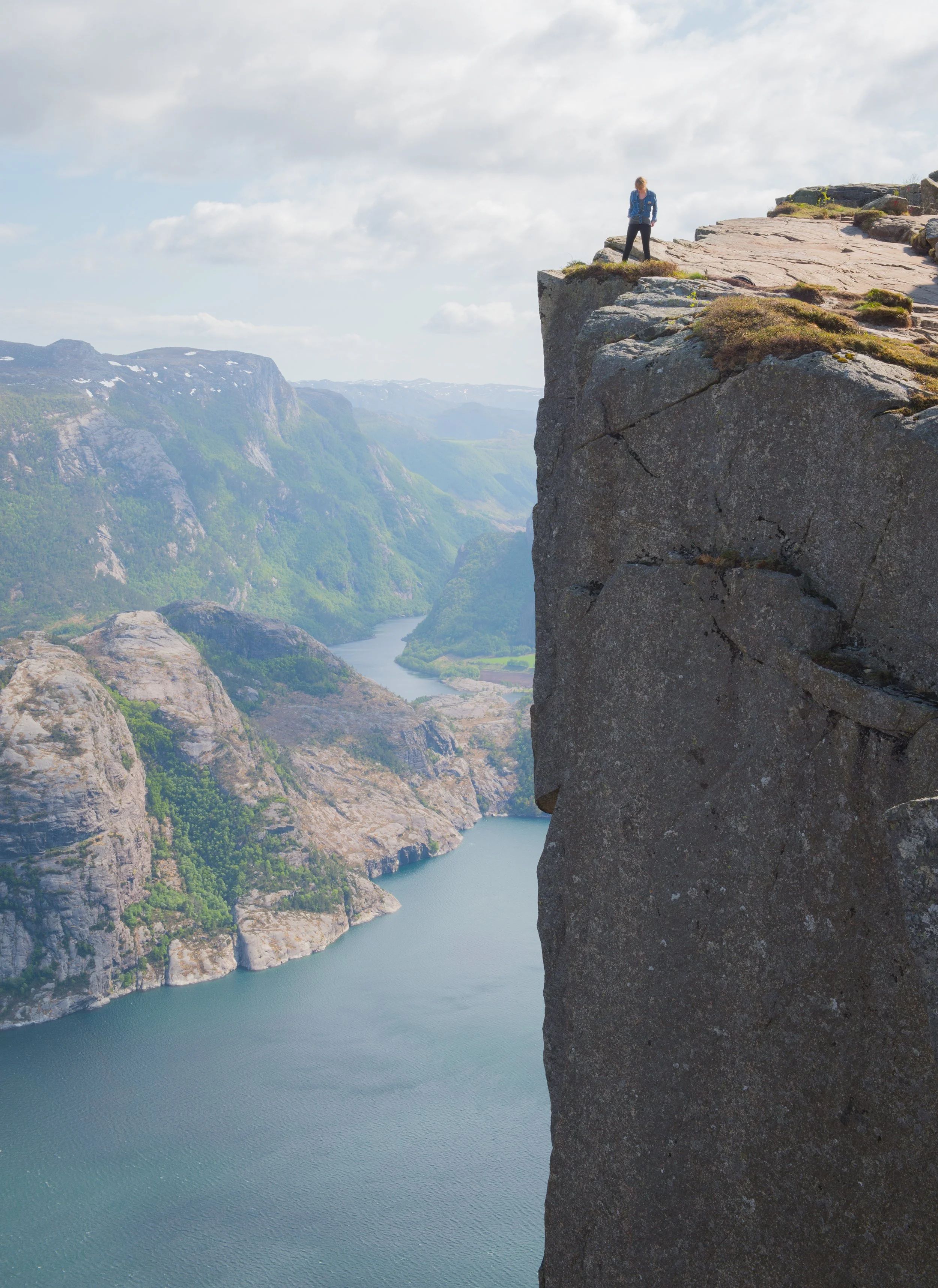 a woman stands on the edge of a cliff overlooking a fjord at preikestolen (pulpit rock) in norway