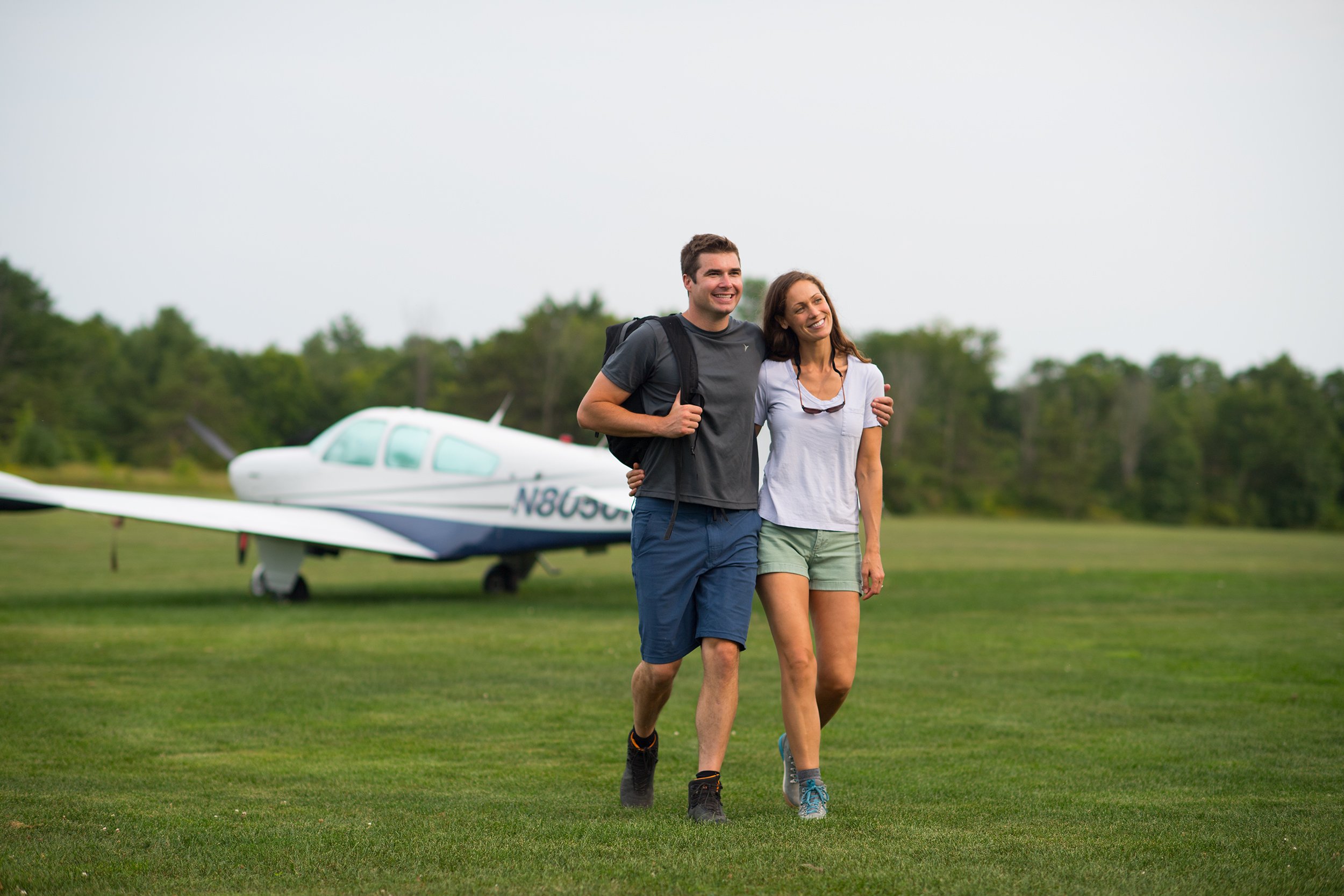 lifestyle photography of a male and female couple walk away from a small airplane on a grass landing strip at basin harbor club in vermont