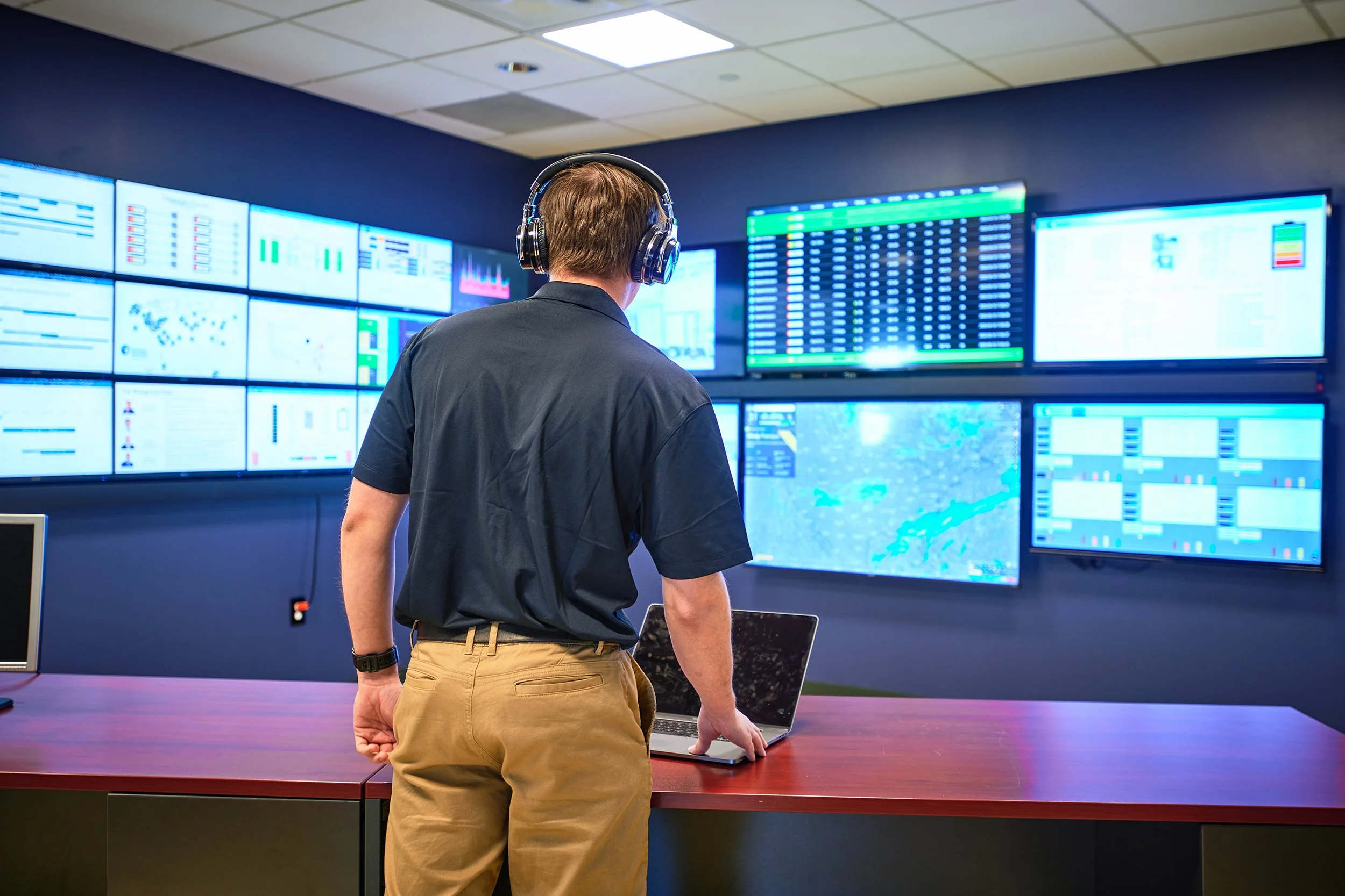 a man stands in front of many television screens in a hi tech control room