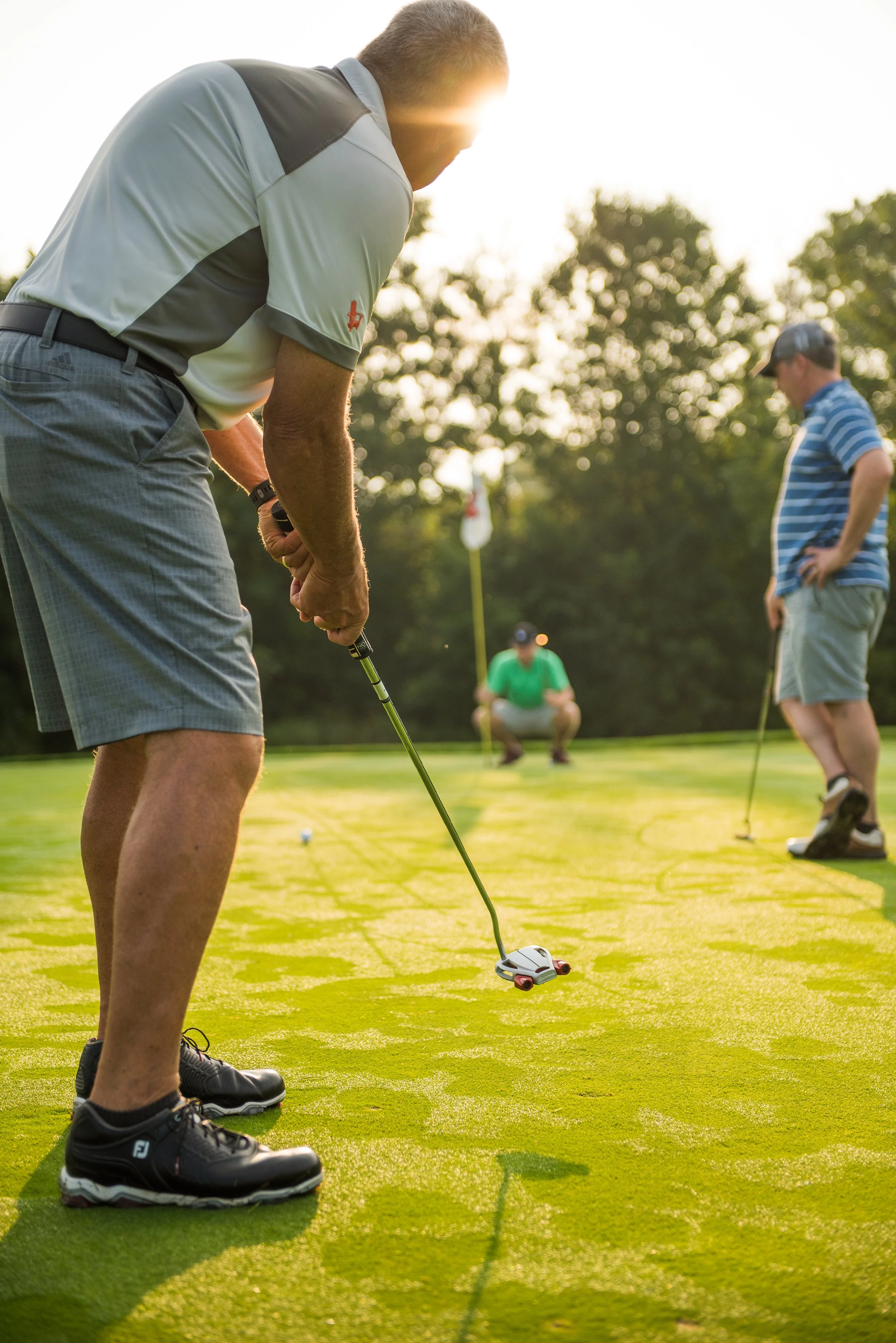 lifestyle photography low angle photo of a man putting while his caddy and friend look on