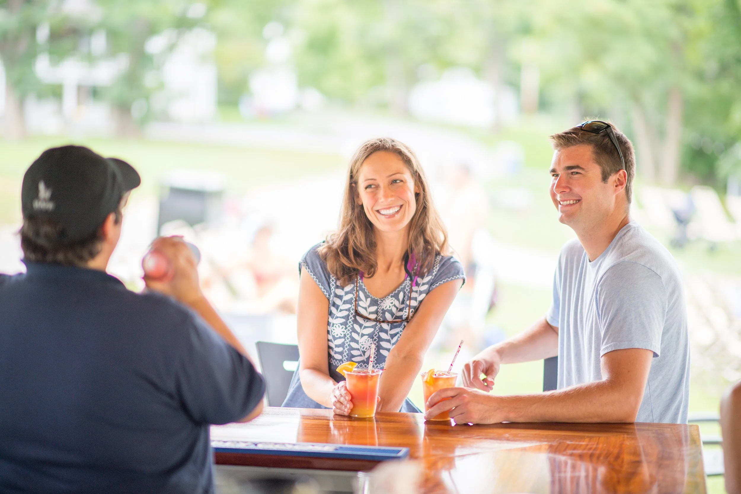 man and woman talk to a bartender while she mixes a cocktail