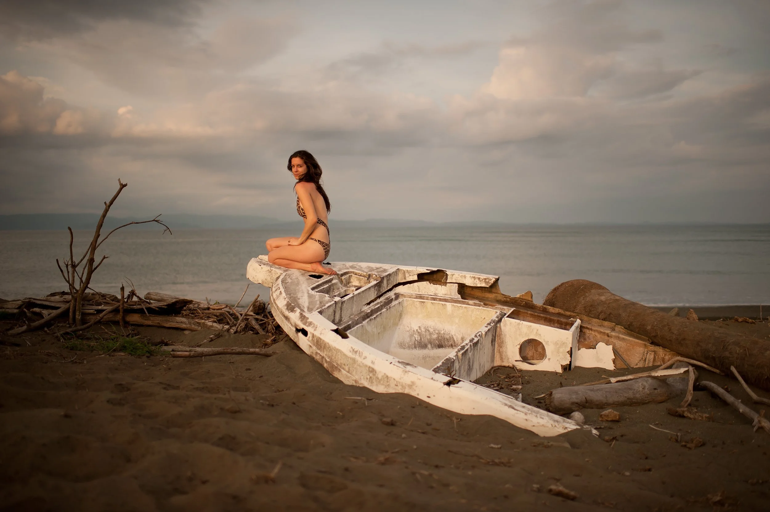 travel photography of woman in bikini sitting on a shipwrecked boat on a remote costa rican beach at sunset