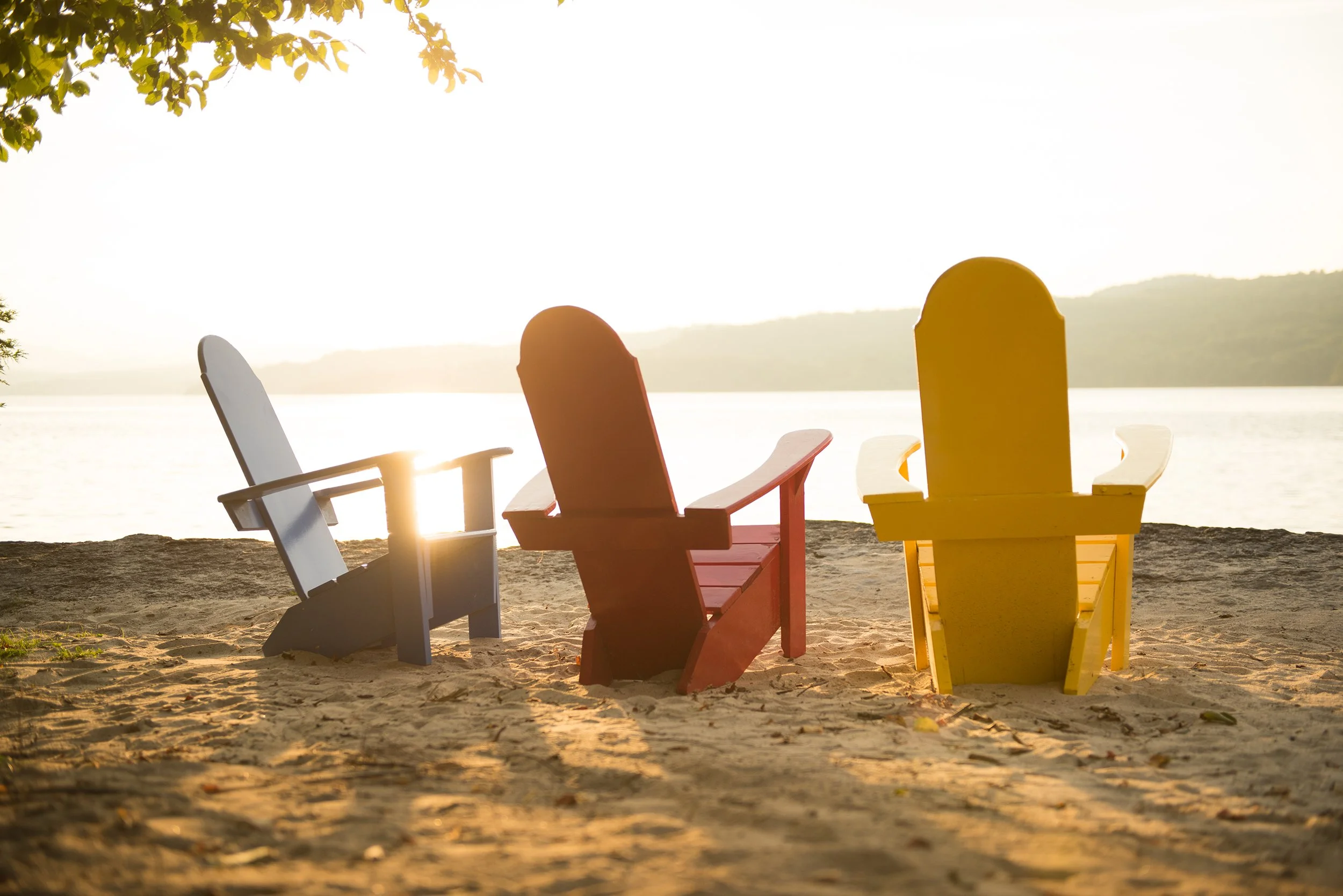 blue, red, and yellow adirondack chairs on a sandy vermont beach at sunset