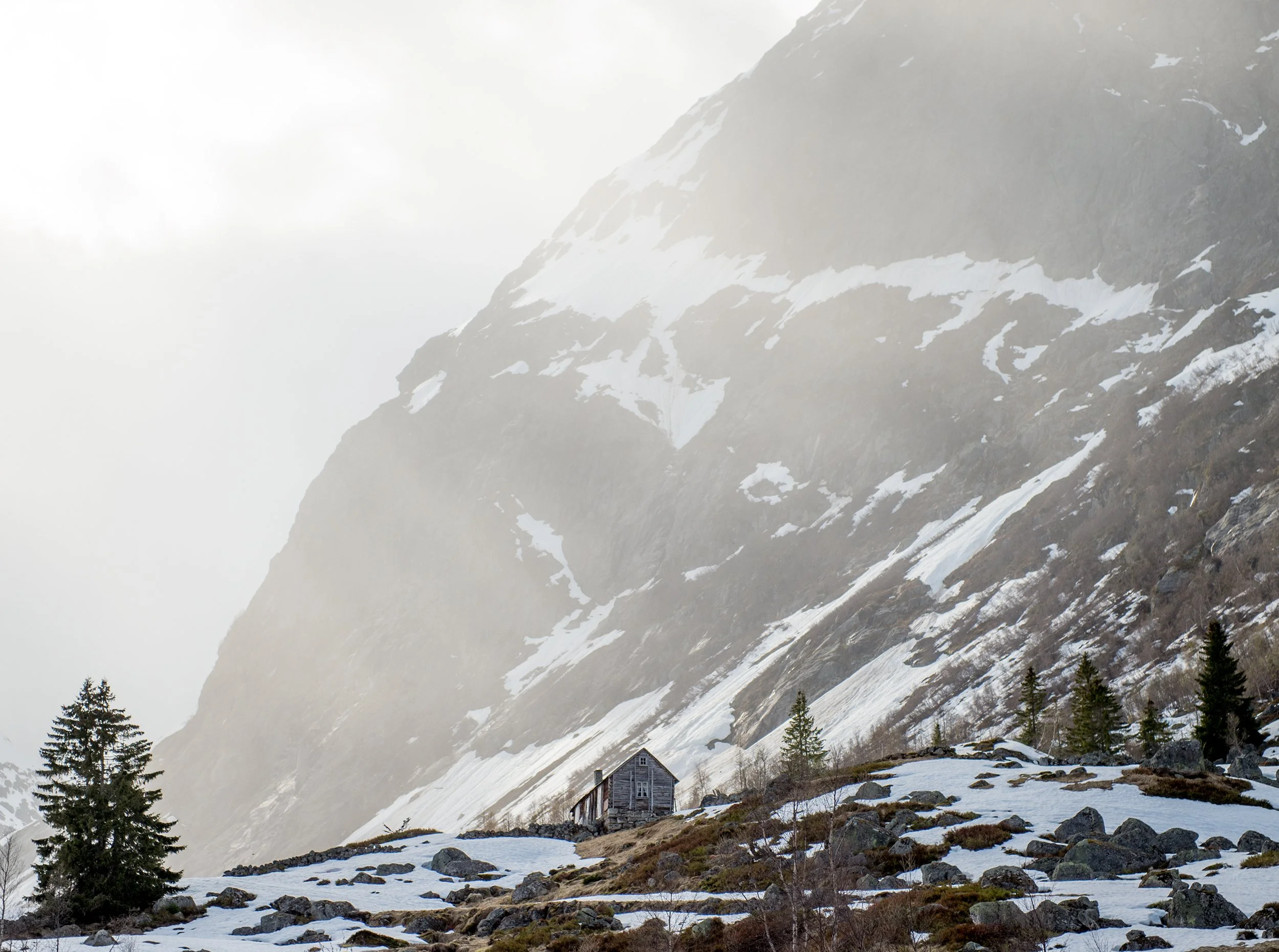 a small cabin surrounded by snowy rocky mountains